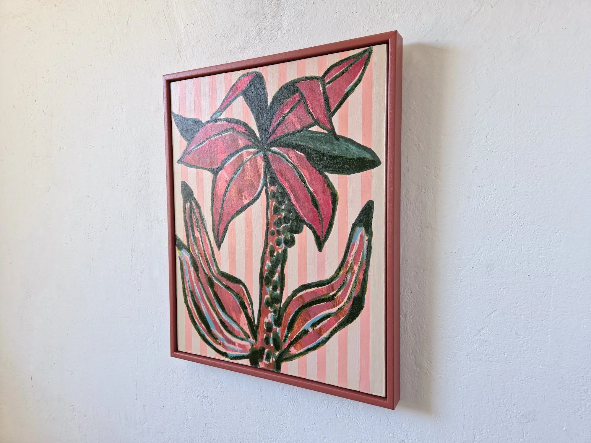 angled view of framed palm tree painting with pink stripes background