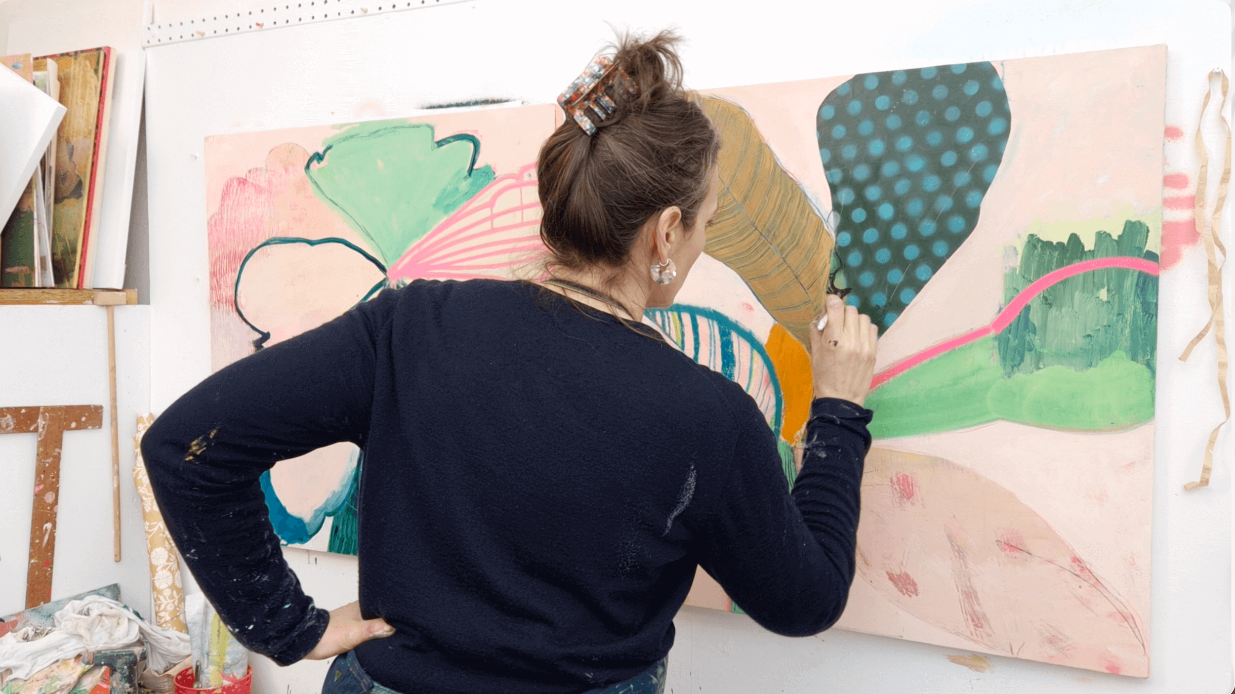 Woman painting a colorful abstract artwork on a large canvas in an art studio.