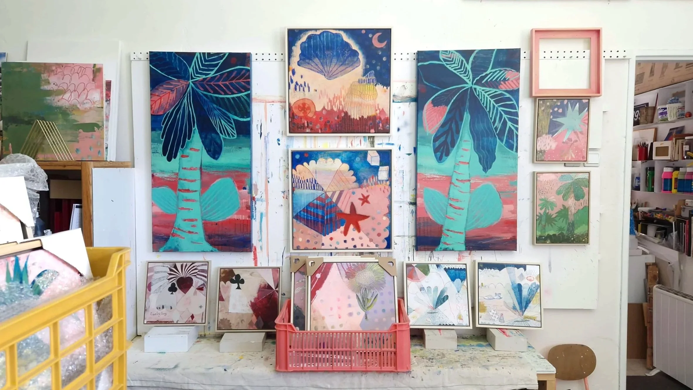 Wall featuring multiple colorful abstract and botanical paintings in an art studio.