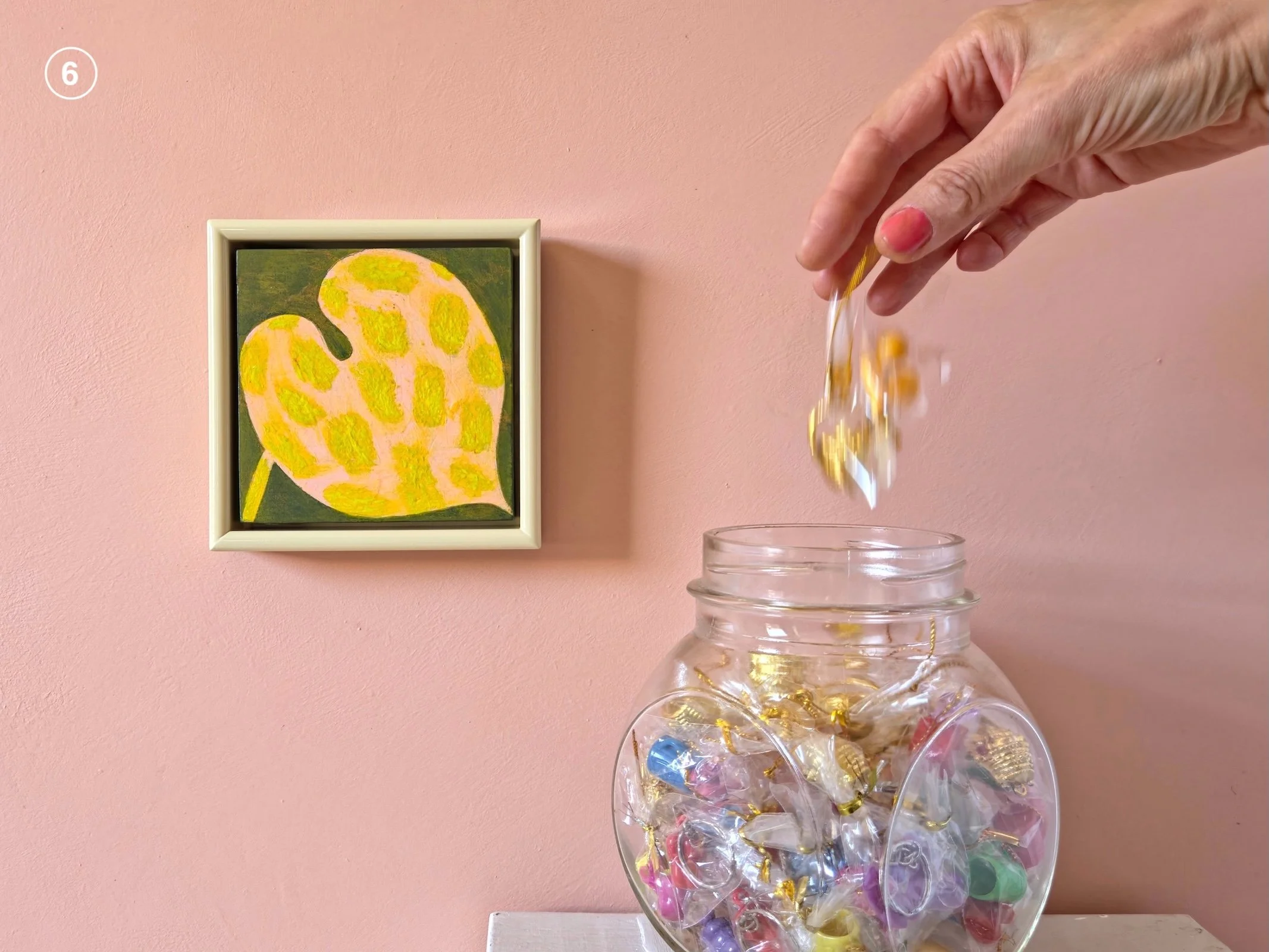 small framed painting of a leaf on a pink wall next to jar of candies