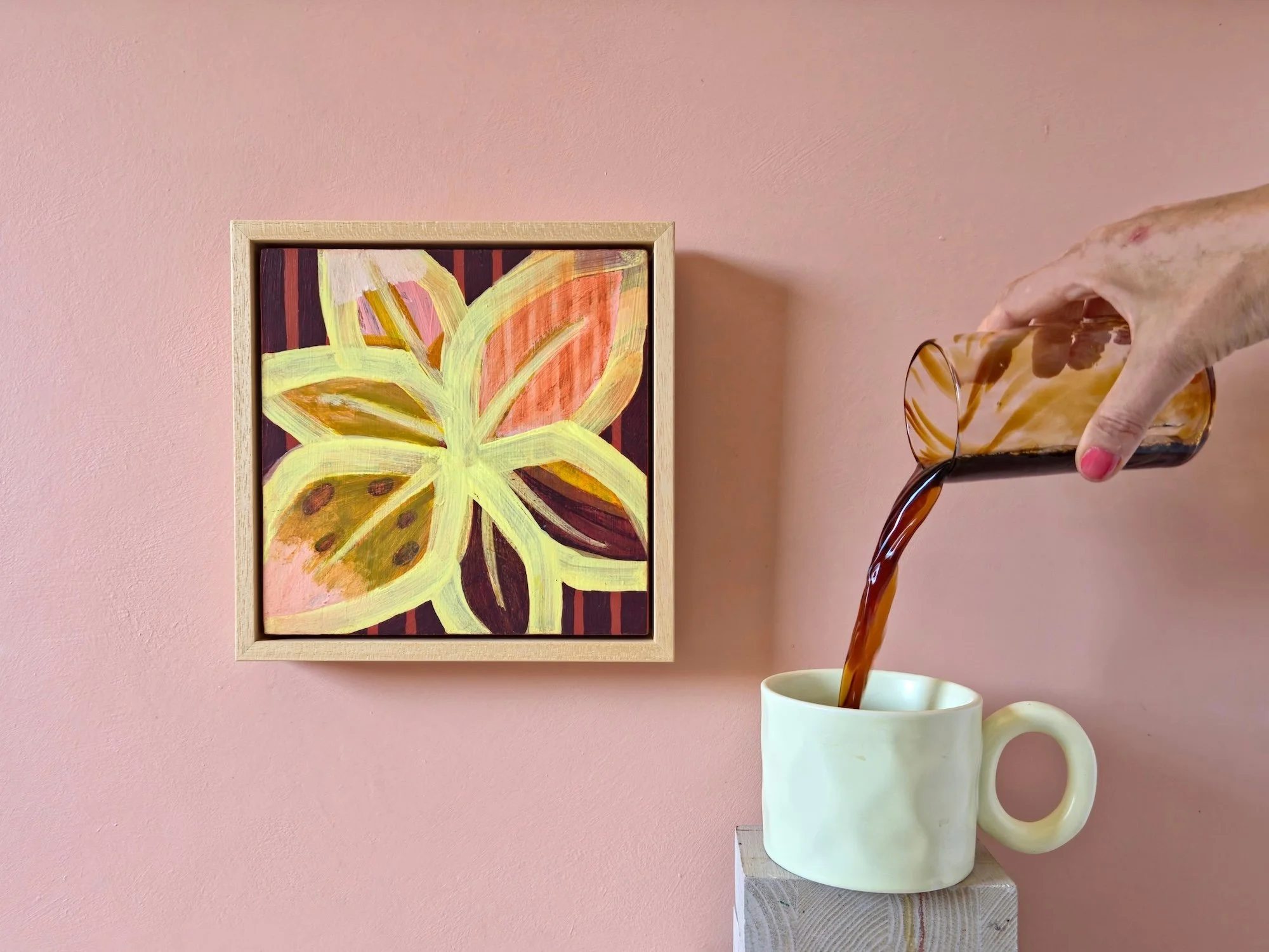 framed botanical painting in pinks, yellows and browns hanged on a pink wall with a cup