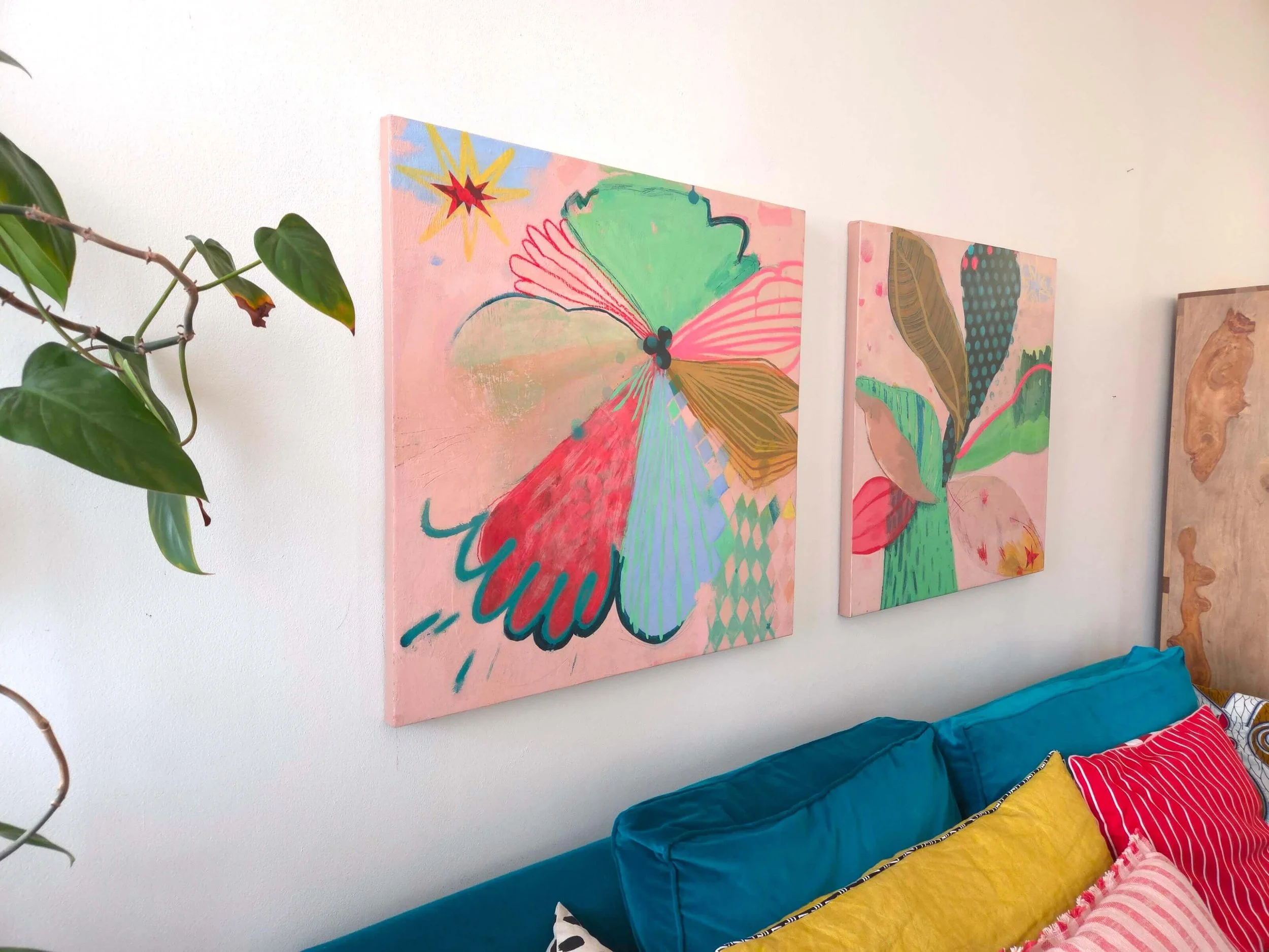 two colourful palm tree paintings hanged above a colourful sofa