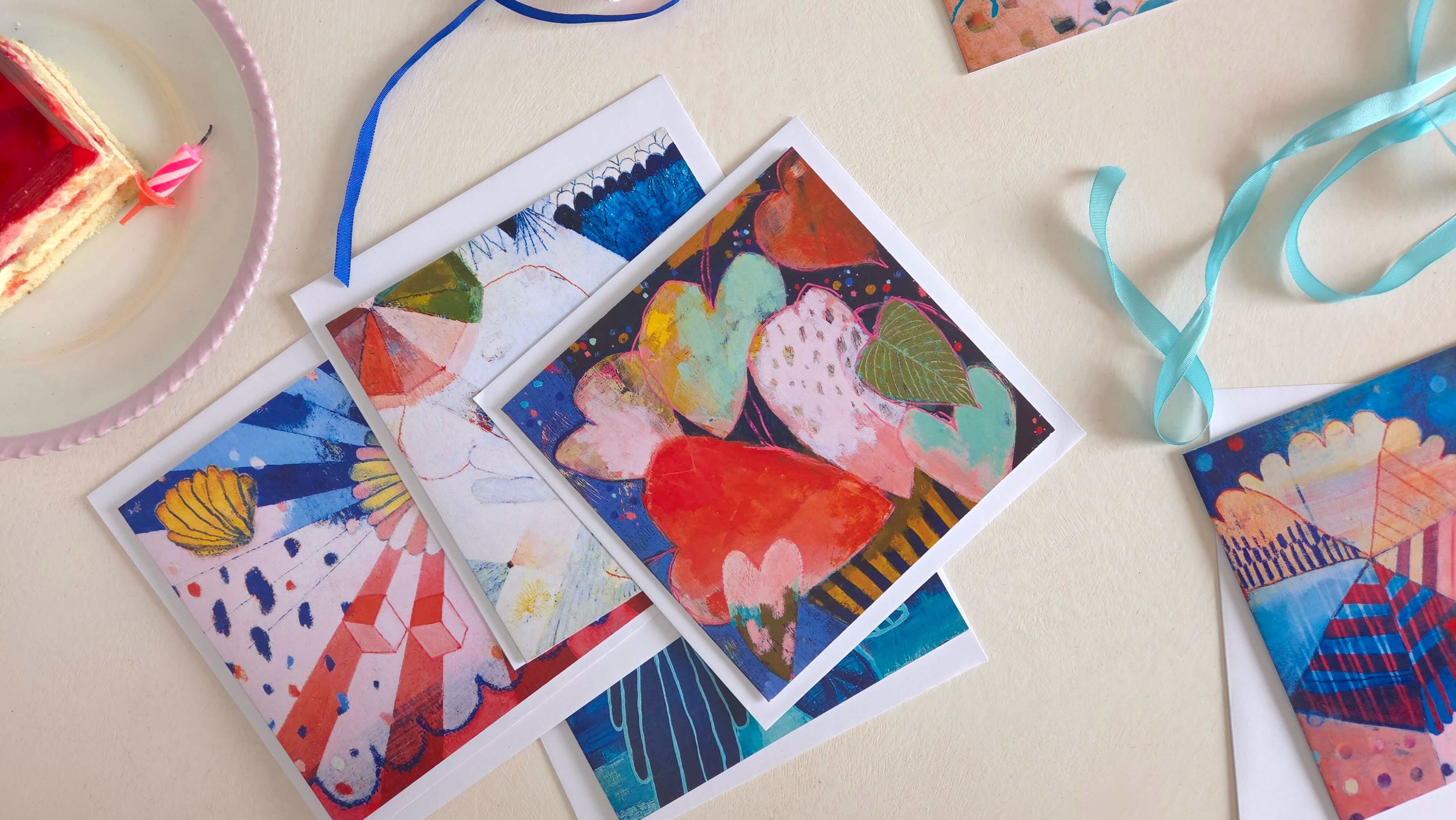 art greeting cards and envelopes on a table, with birthday cake and blue ribbon