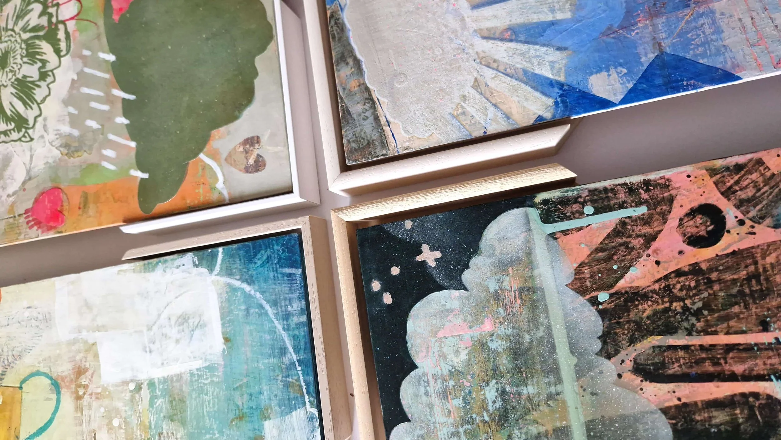 Close-up of four framed abstract paintings with vibrant colors and textured surfaces, with frame samples to be chosen