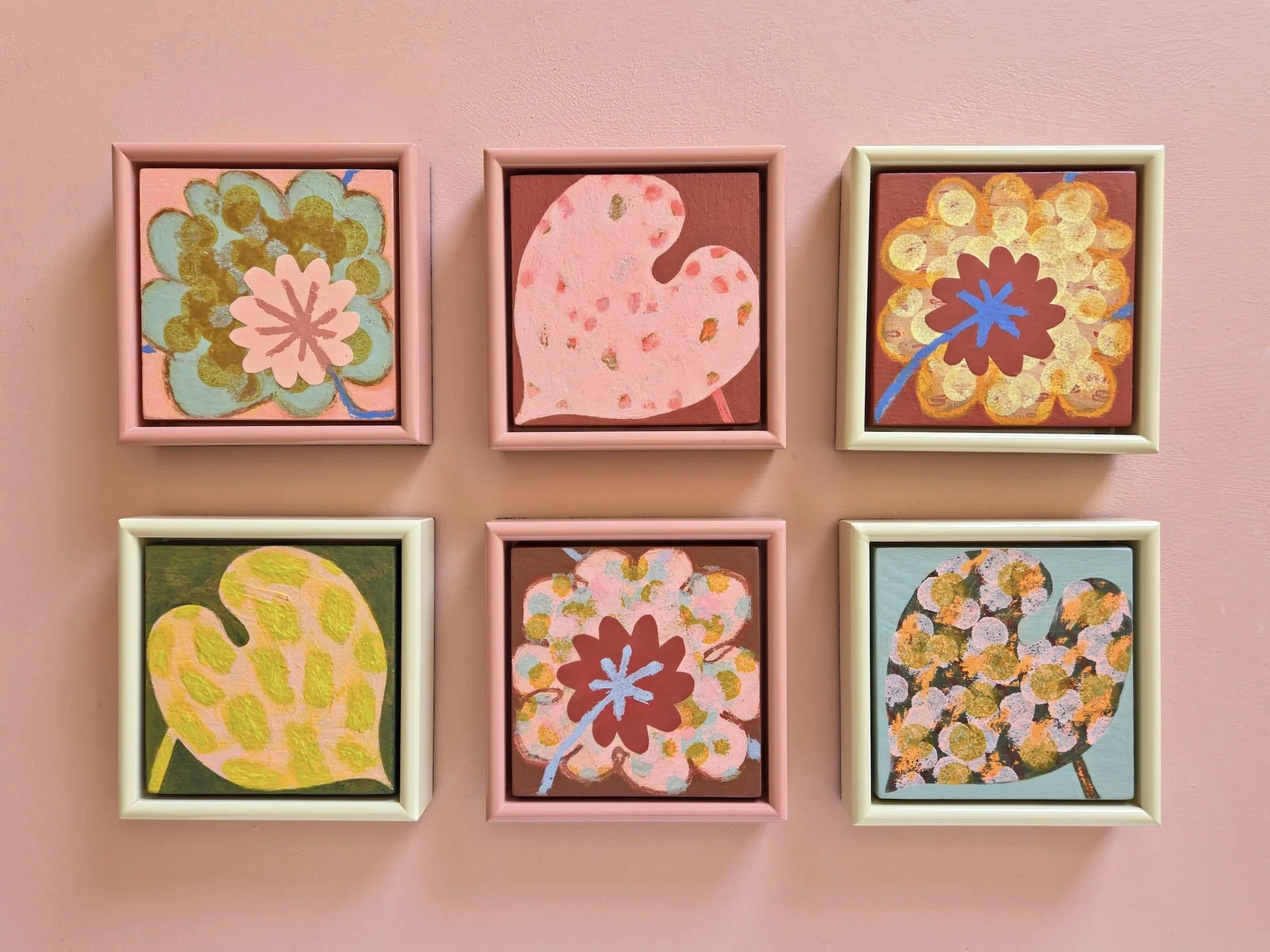six small framed botanical paintings on a pink wall