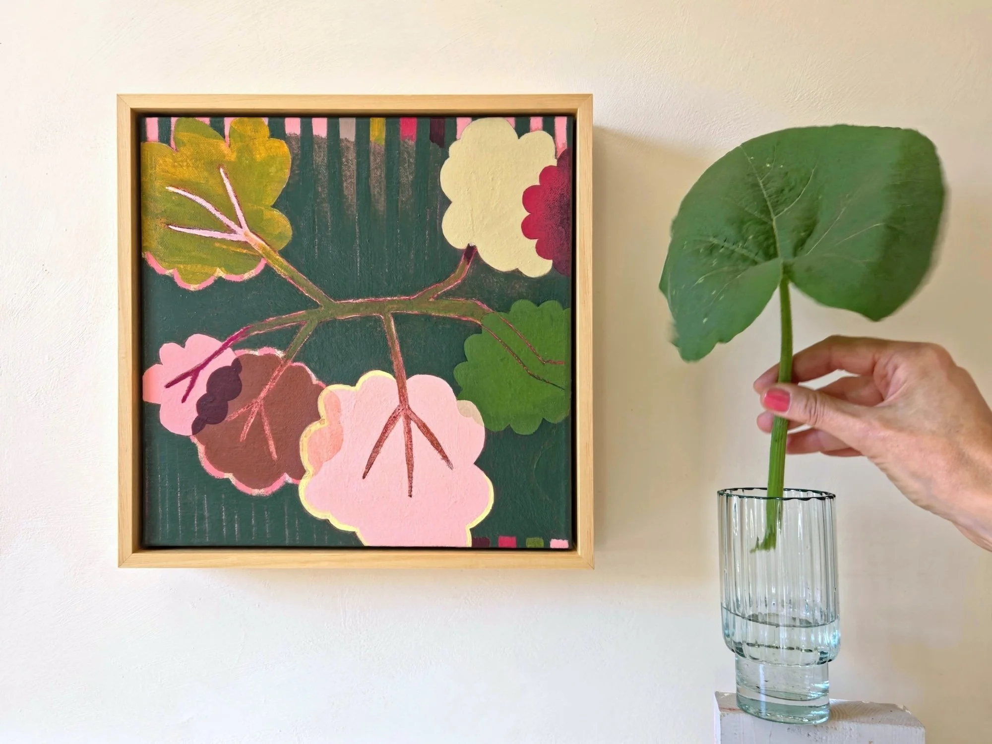 framed botanical painting in pinks and greens with a vase and a big green leaf