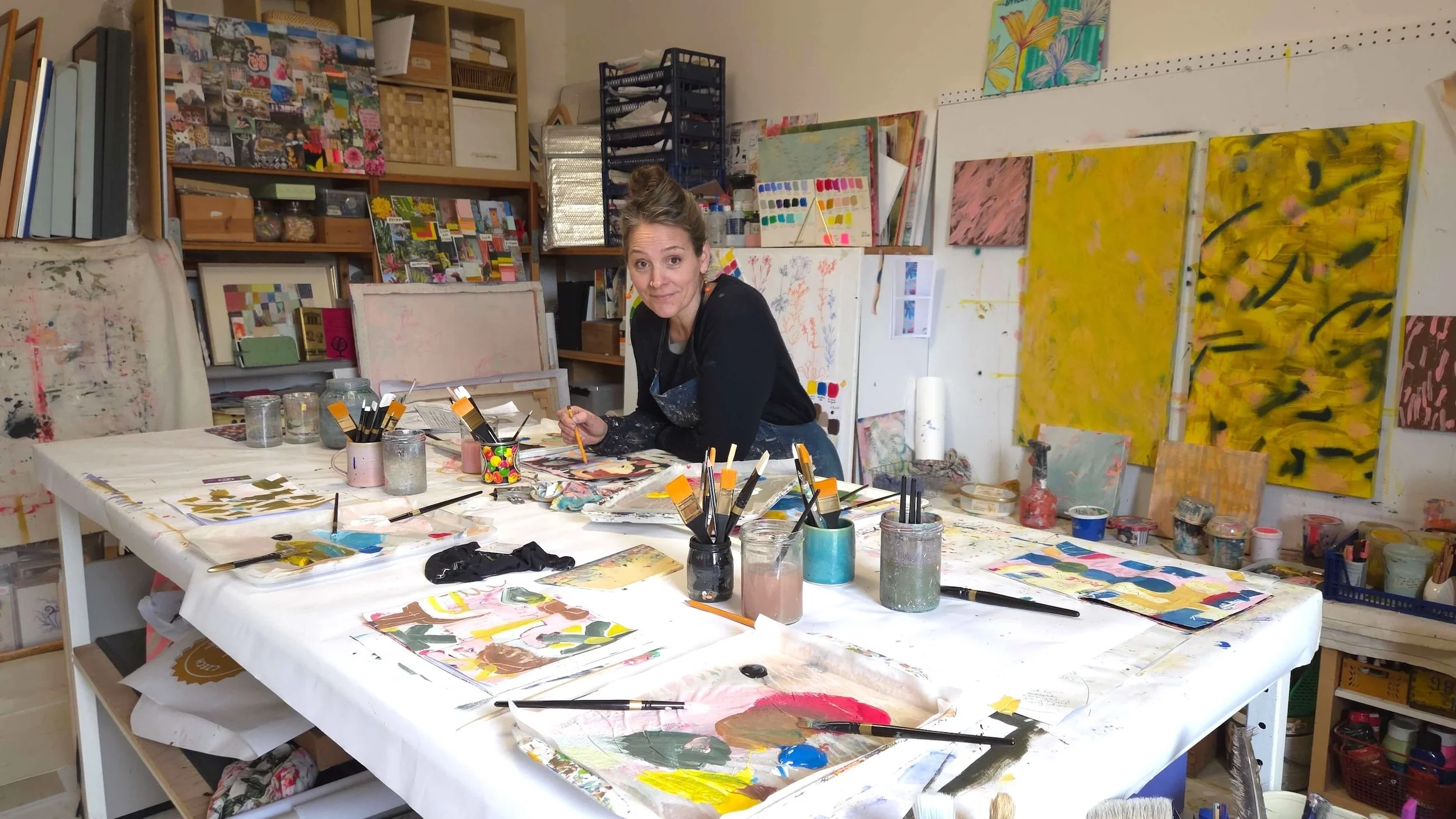 Artist at her table covered with painting material, palettes, brushes and sketchbooks