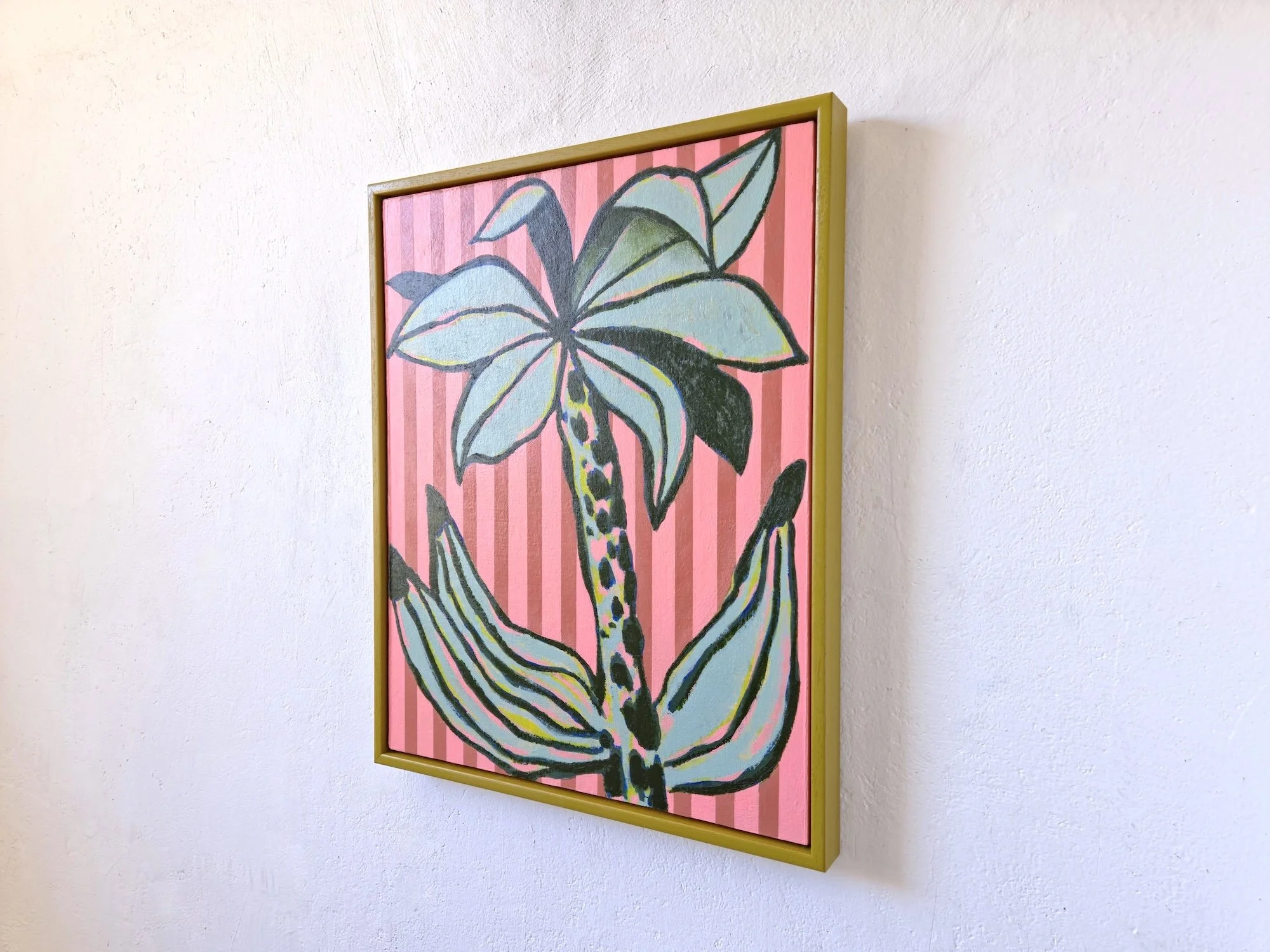 angled view of framed palm tree painting with pink striped background