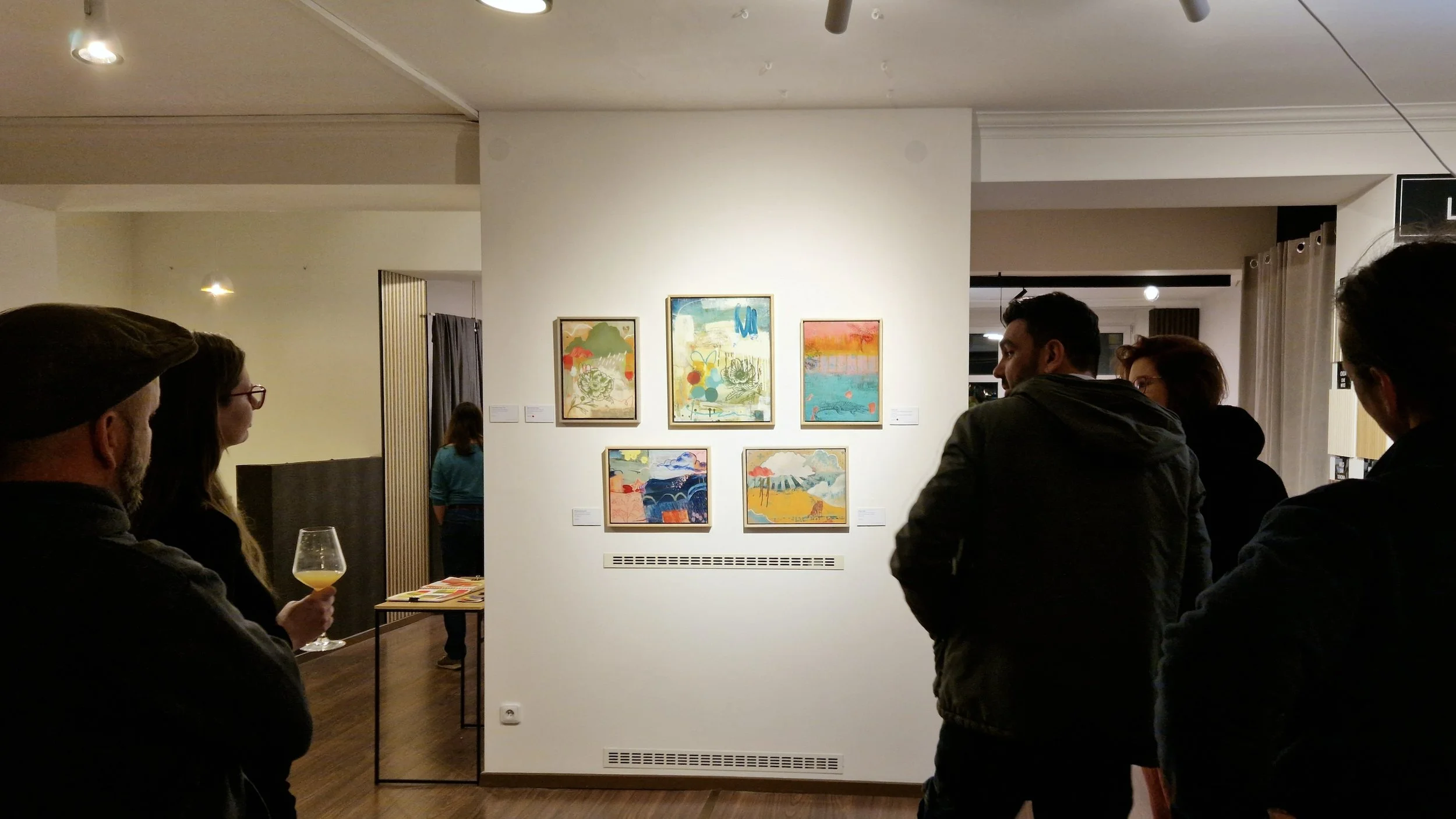 Visitors in front of mixed media paintings on the opening night of a solo artist show