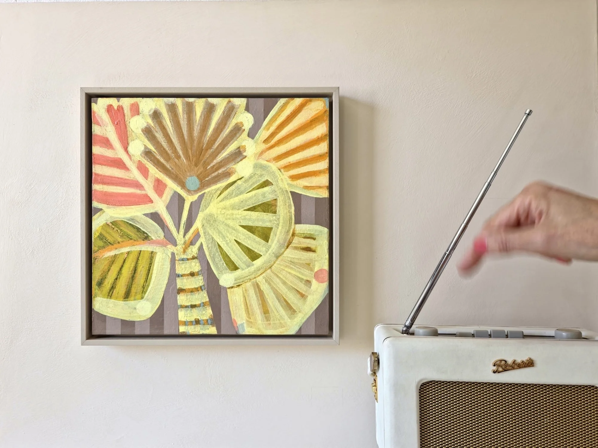 framed palm tree painting in bright yellows and pinks hanged on a white wall next to a retro radio