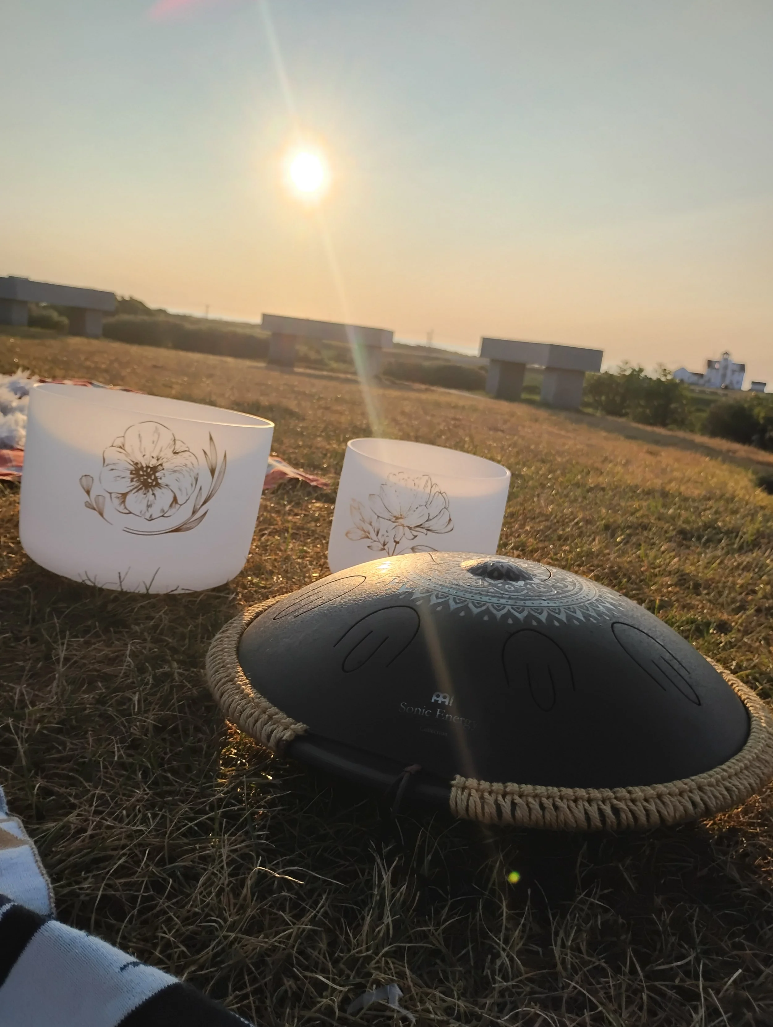 Glowing sunrise upon crystal singing bowls and a tongue drum sitting in a grassy field