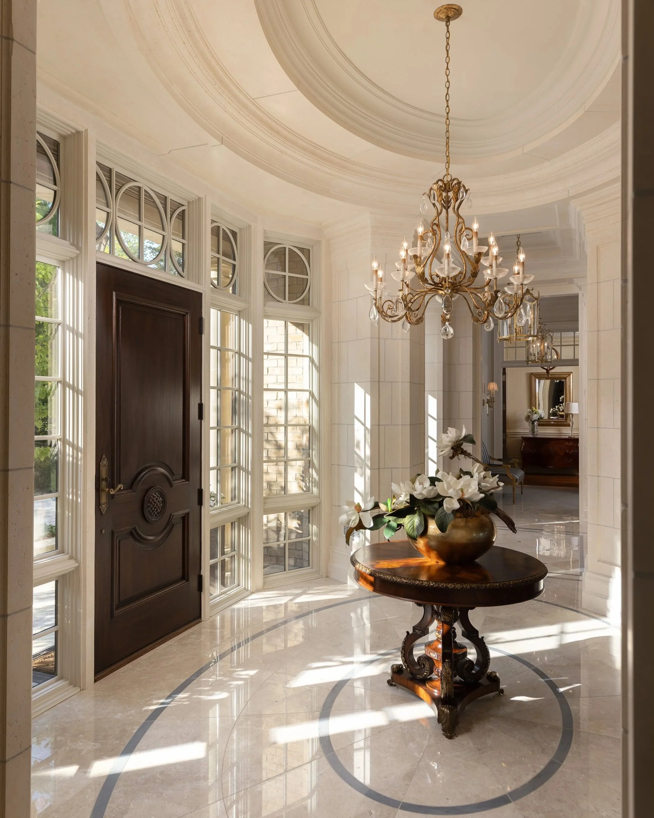 $40m home. Elegant foyer with large windows, a wooden door, a chandelier, and a round table with a flower arrangement.
