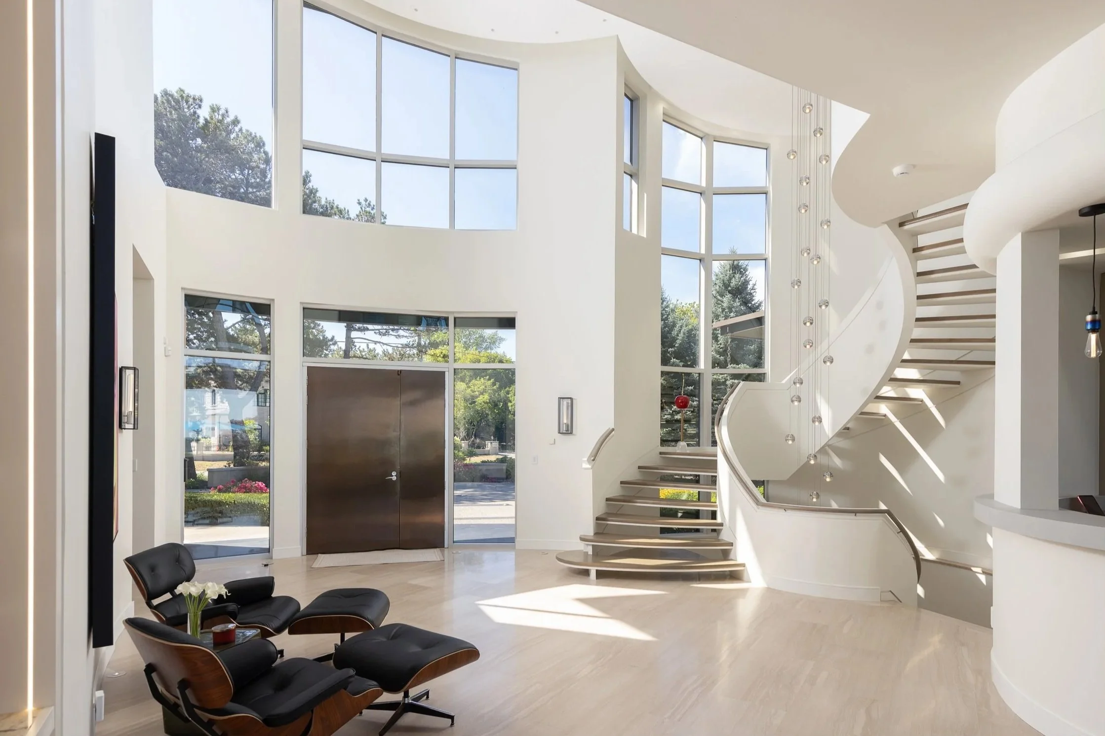 Modern staircase with a glass railing in a spacious, bright lobby with large windows and minimalistic furnishings.