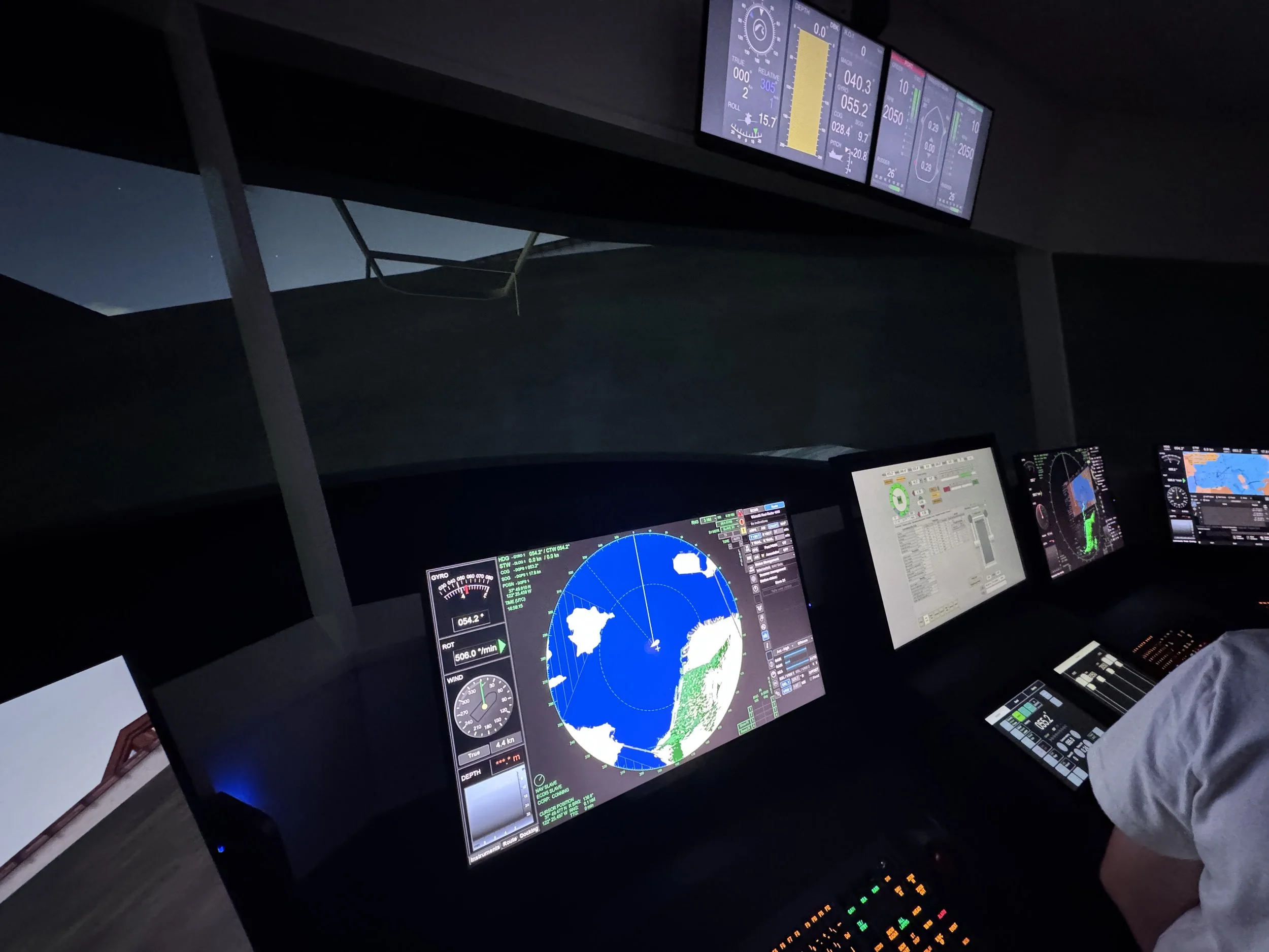 Multiple computer screens displaying flight instruments, navigation maps, and data, set in an aircraft cockpit at night.