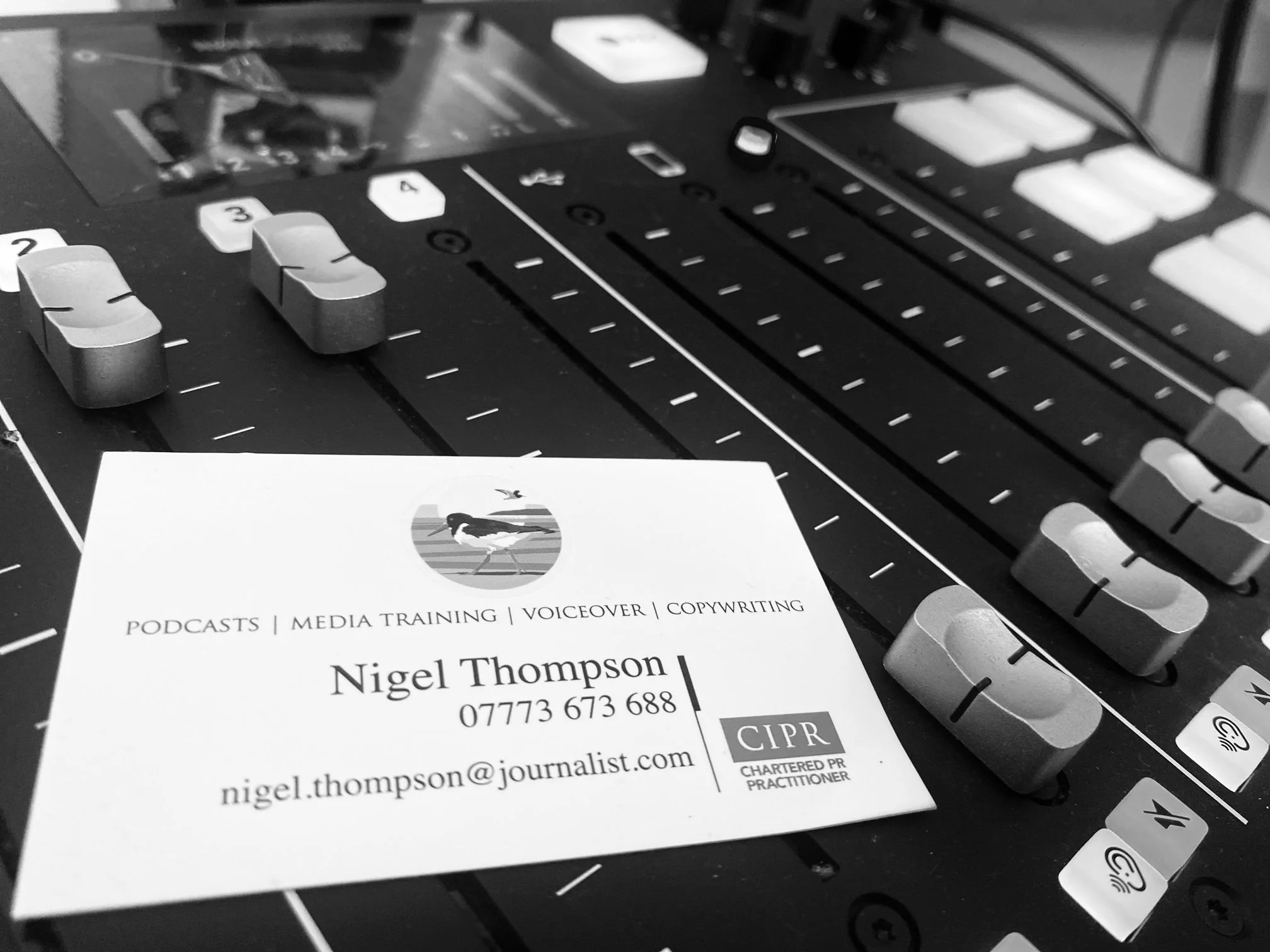 A business card for Nigel Thompson, a journalist and media professional, resting on an audio mixing console.