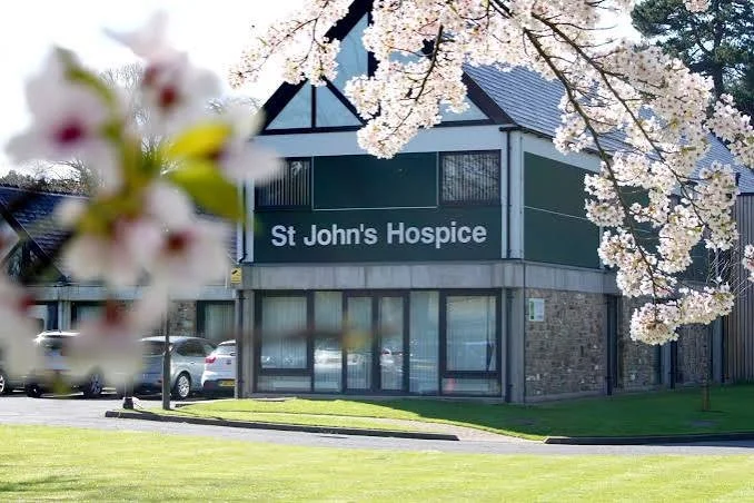 Building with sign that reads 'St John's Hospice' surrounded by cherry blossom trees in bloom.