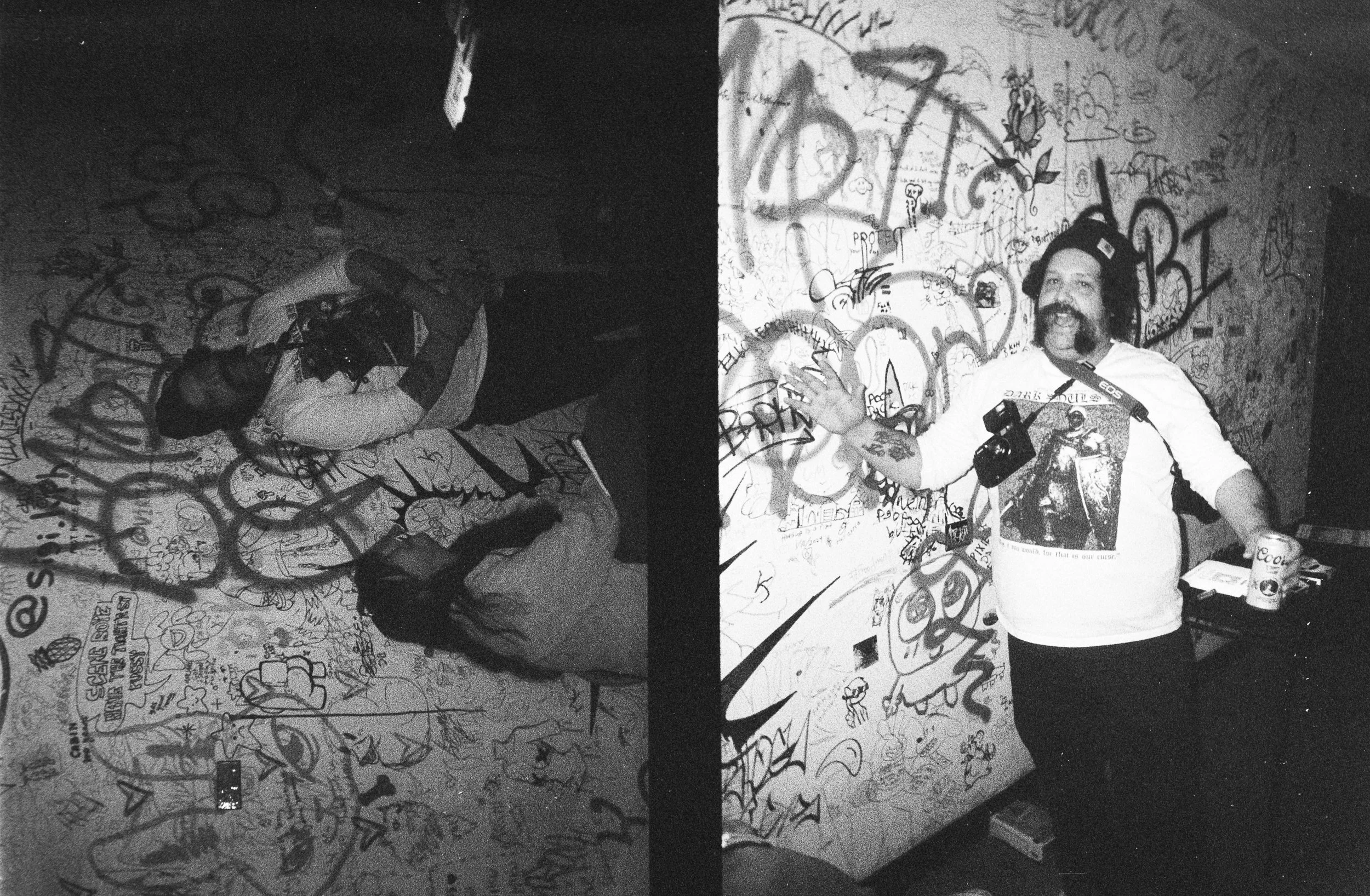 A black and white split image showing a woman and a man in a graffiti-covered room. The woman, on the left, has long hair, glasses, and is wearing a scarf, standing against the graffiti wall with her arms crossed. The man, on the right, with a beard 