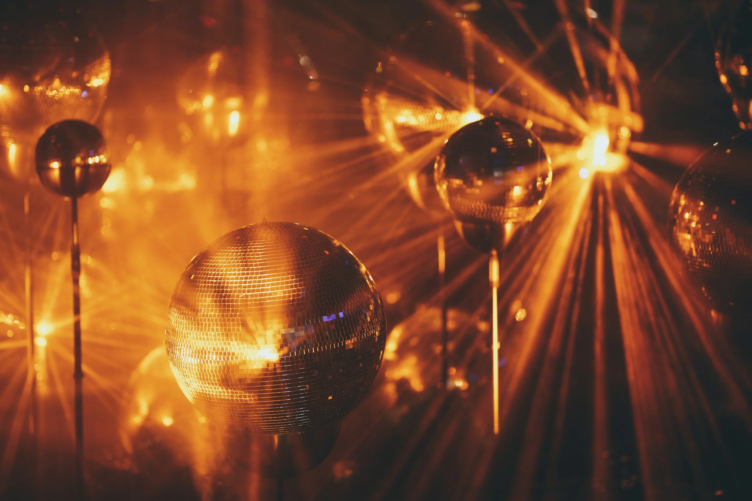 Multiple reflective disco balls illuminated by orange and gold lights, creating a sparkling, vibrant atmosphere.