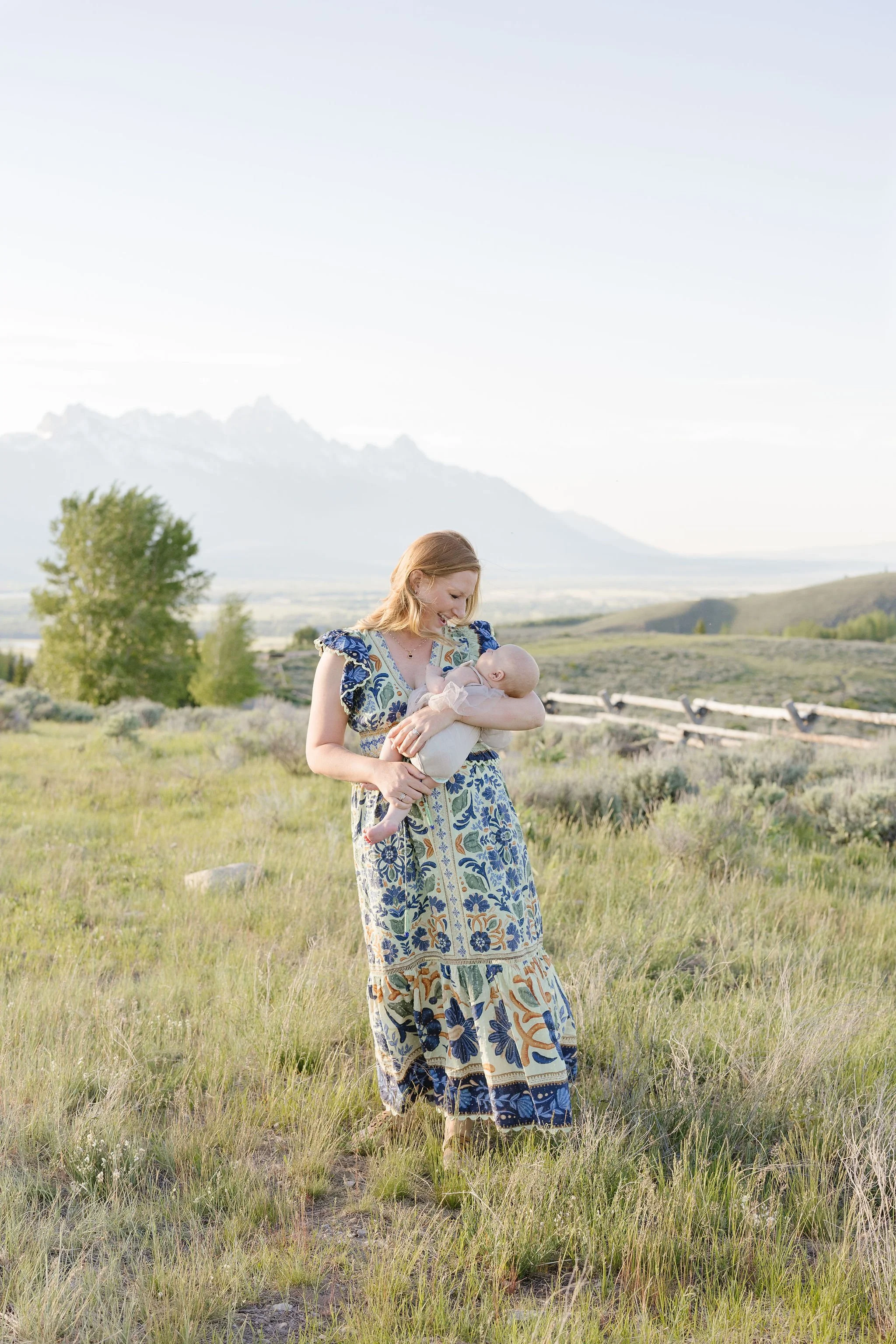 Mother holds baby with the Grand Tetons towering behind them.