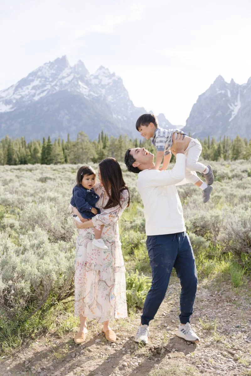  Parents holding their children with a field and mountain background. 