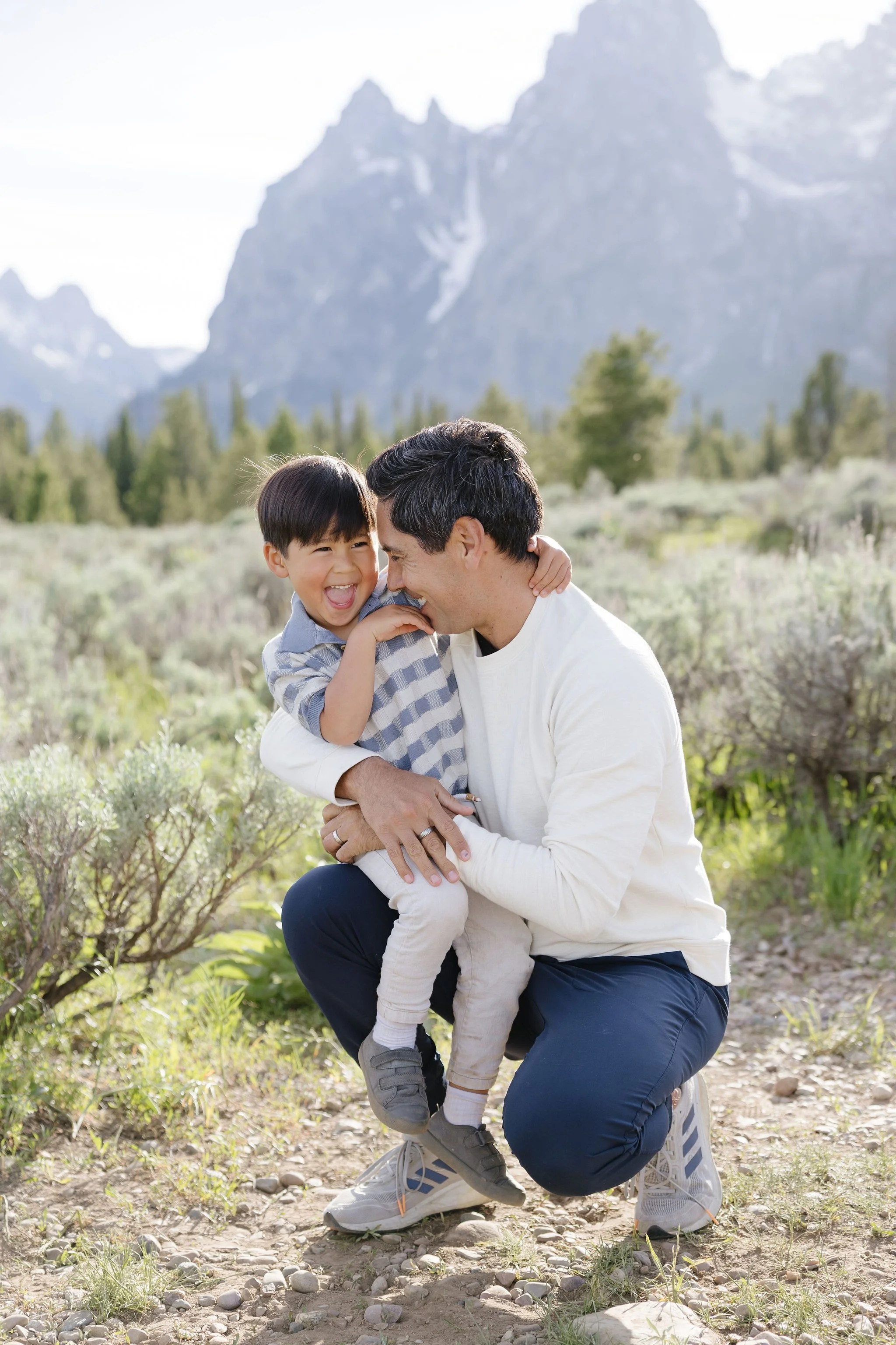  Father kneels as he holds son for photo in the Grand Tetons. 