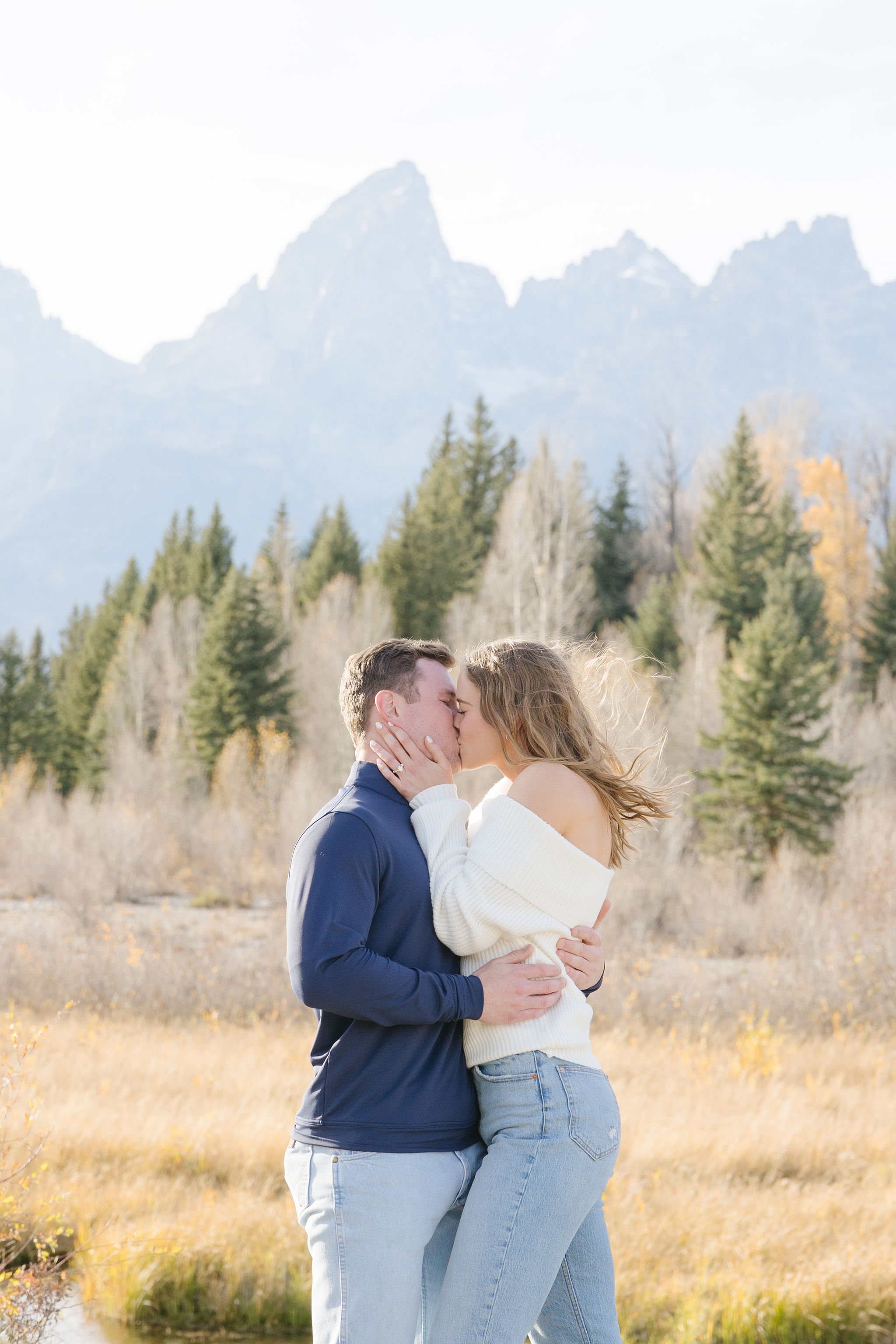  Couple shares kiss in Grand Teton National Park with mountain views in the background. 