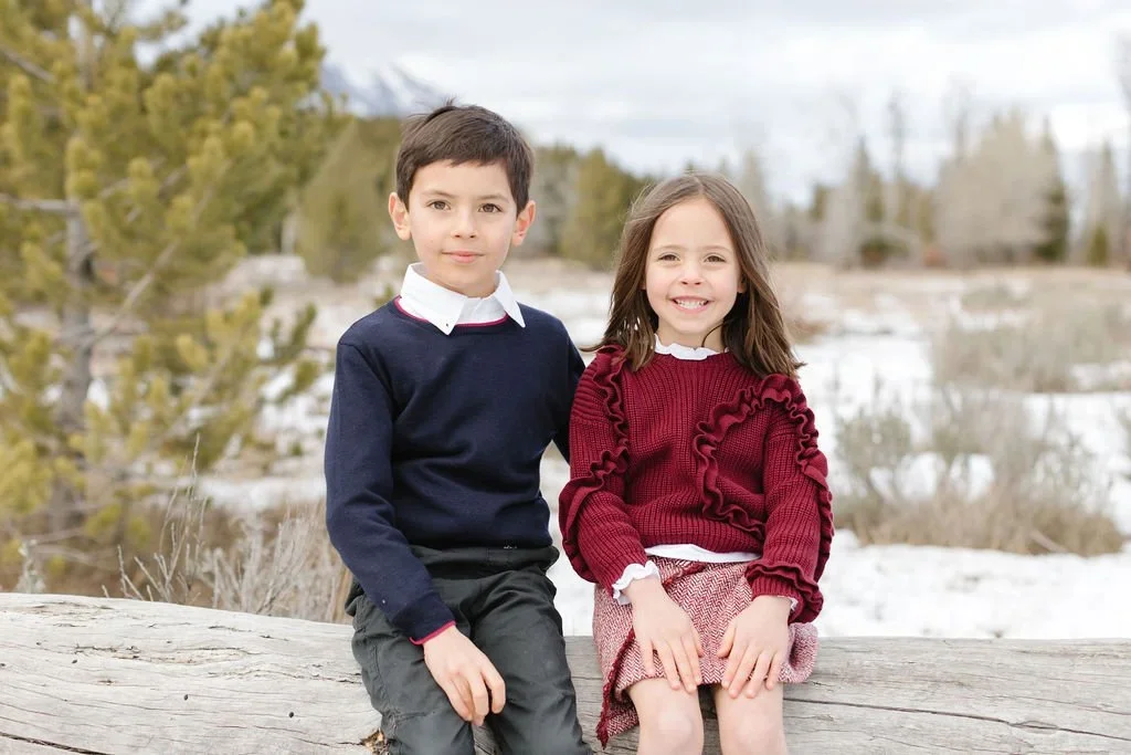  Brother and sister sit on fallen log together during their holiday card photoshoot. 