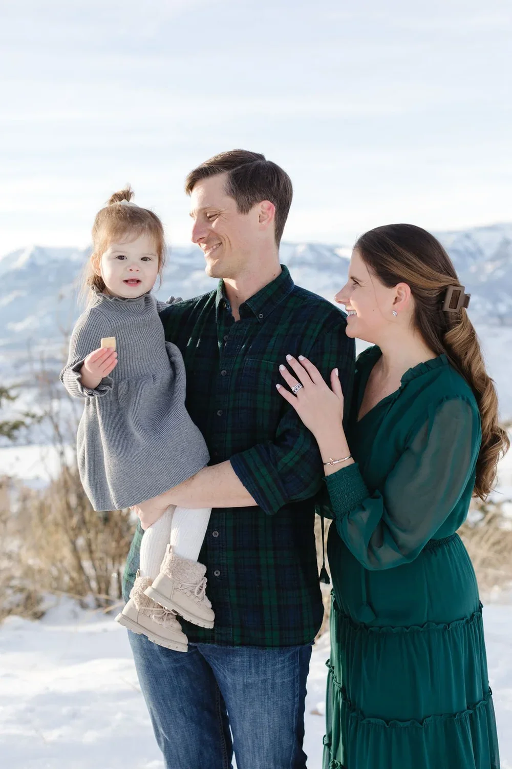  Father holds young daughter as mother rests her hand on his dad’s arm during photoshoot in the snow. 