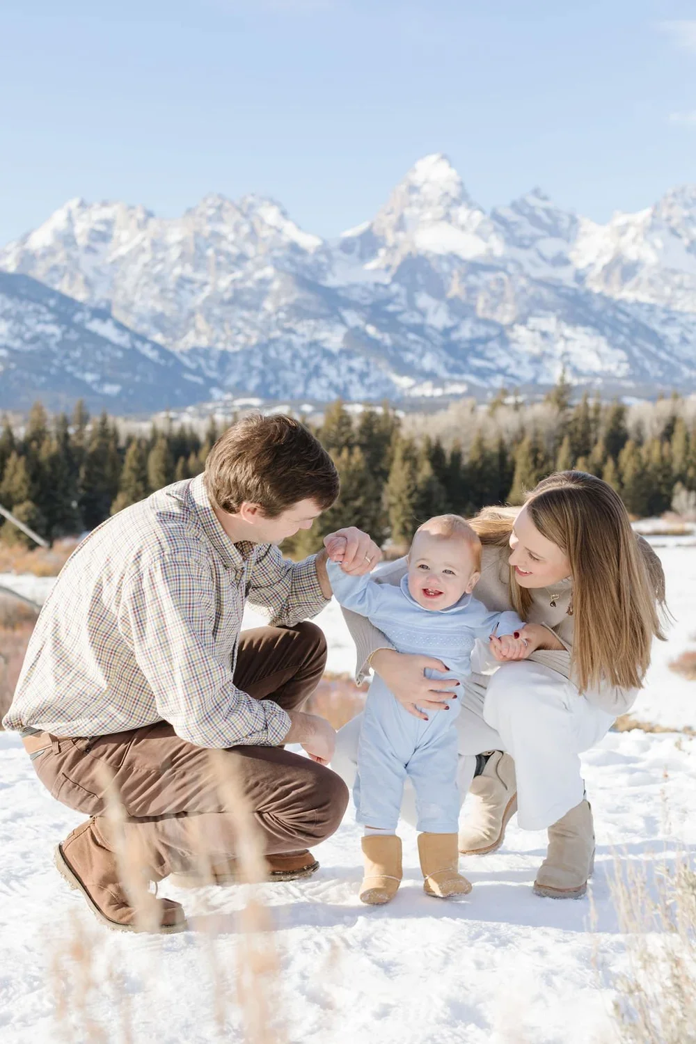  Mother and father bend down in the snow to play with their baby during a holiday card photoshoot in Jackson Hole. 