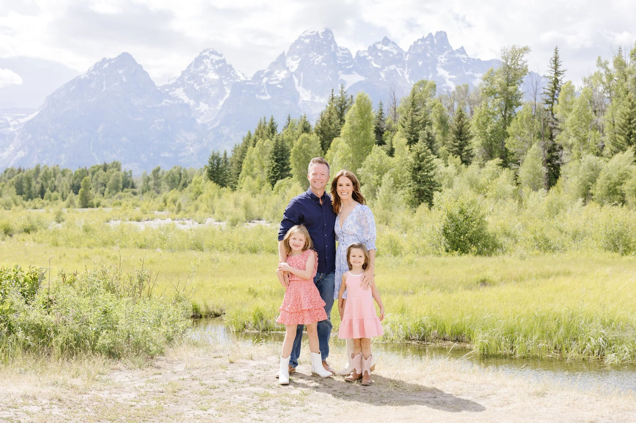  Family stands together for a posed photo with the Teton mountain range behind them. 