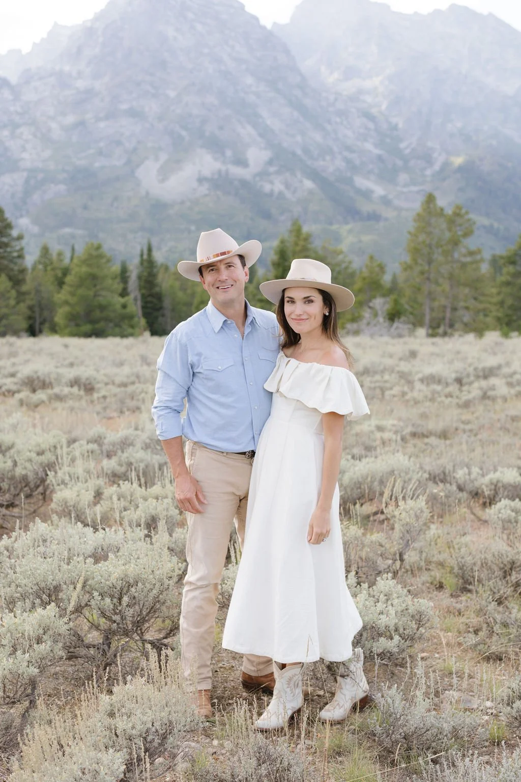  Man and woman stand in field with the Teton mountains behind them. 