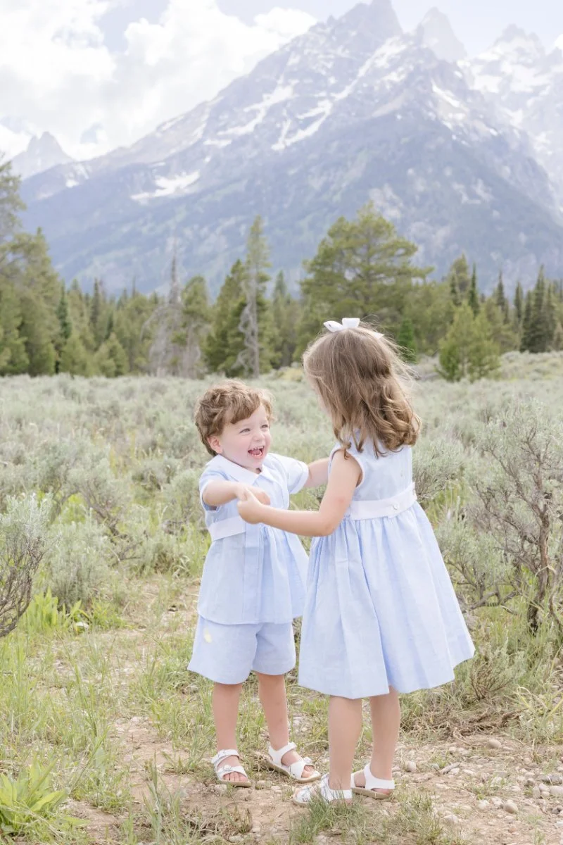  Two young siblings holding hands and dancing together in a field in Jackson Hole. 