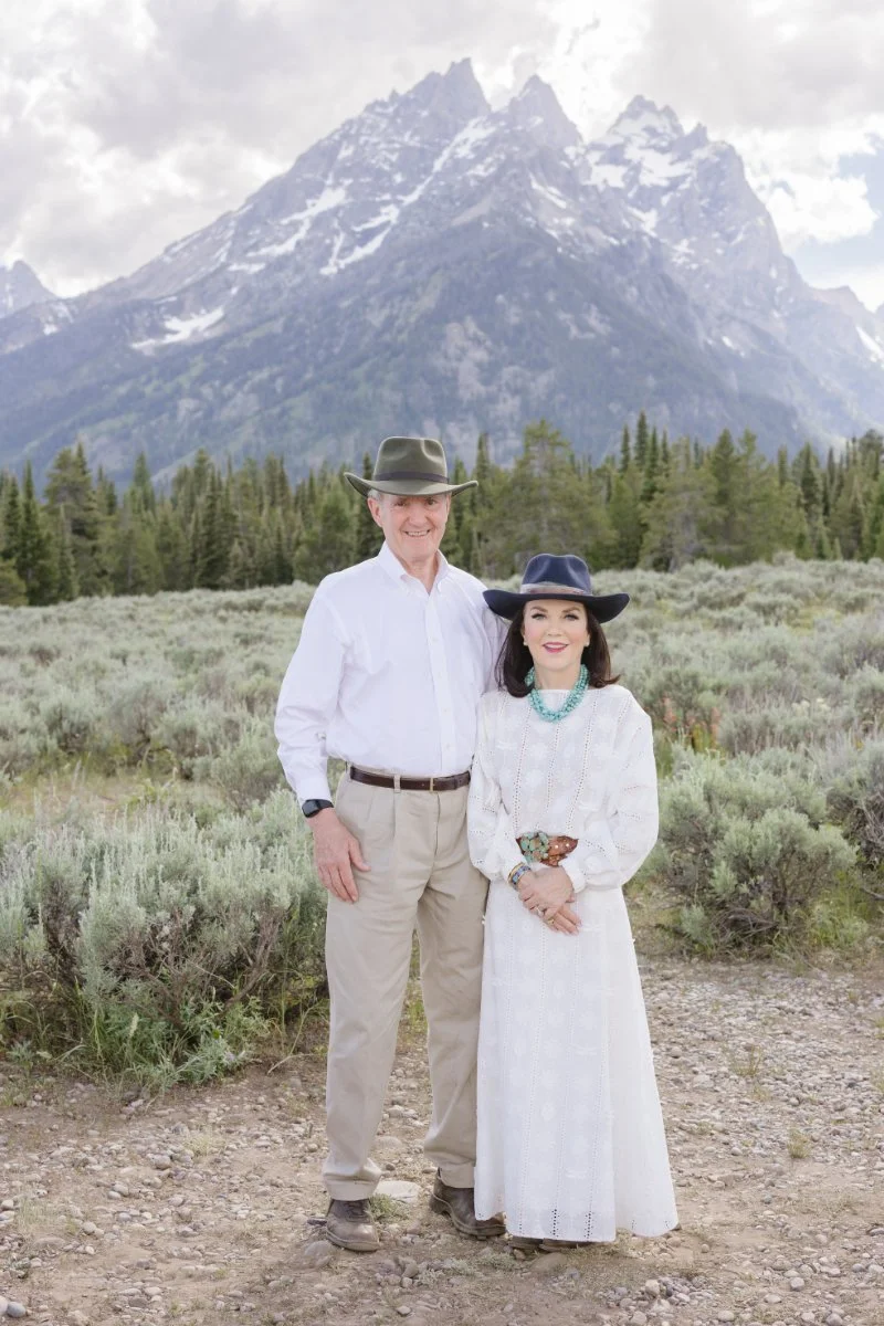  Husband and wife stand facing the photographer fora photo along going-to-the-sun road Montana. 