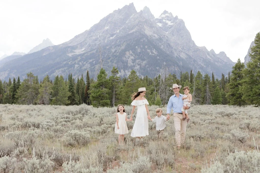  Family stands together holding hands in the Tetons as a photographer captures their family photos. 
