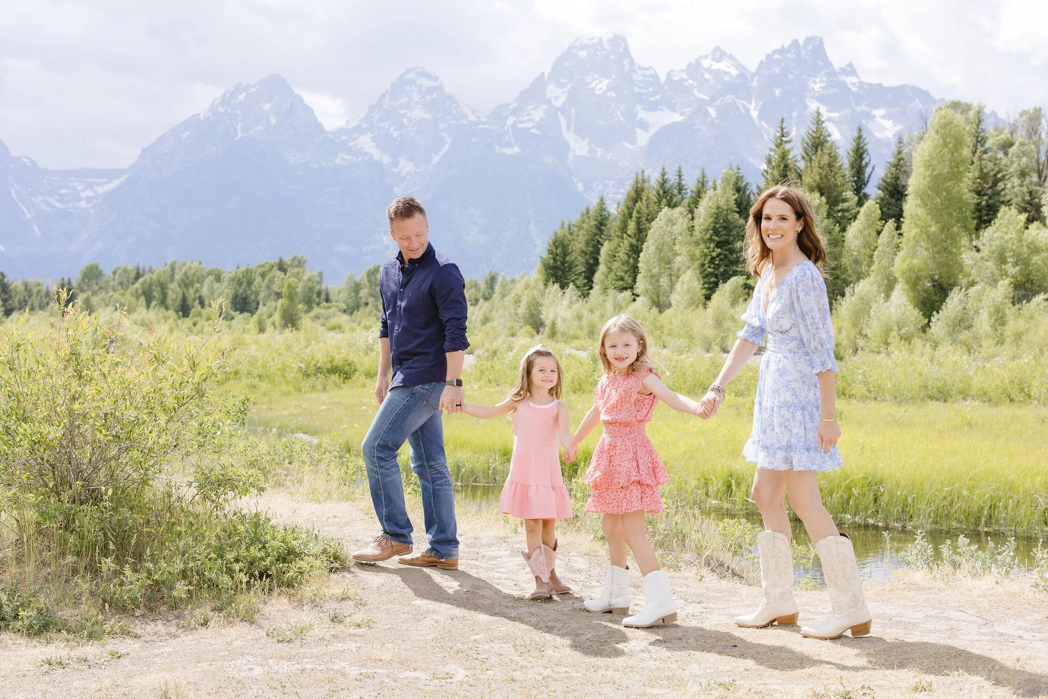Family of four walk together hand in hand with dad leading as Jackson Hole photographers capture them in the Tetons.