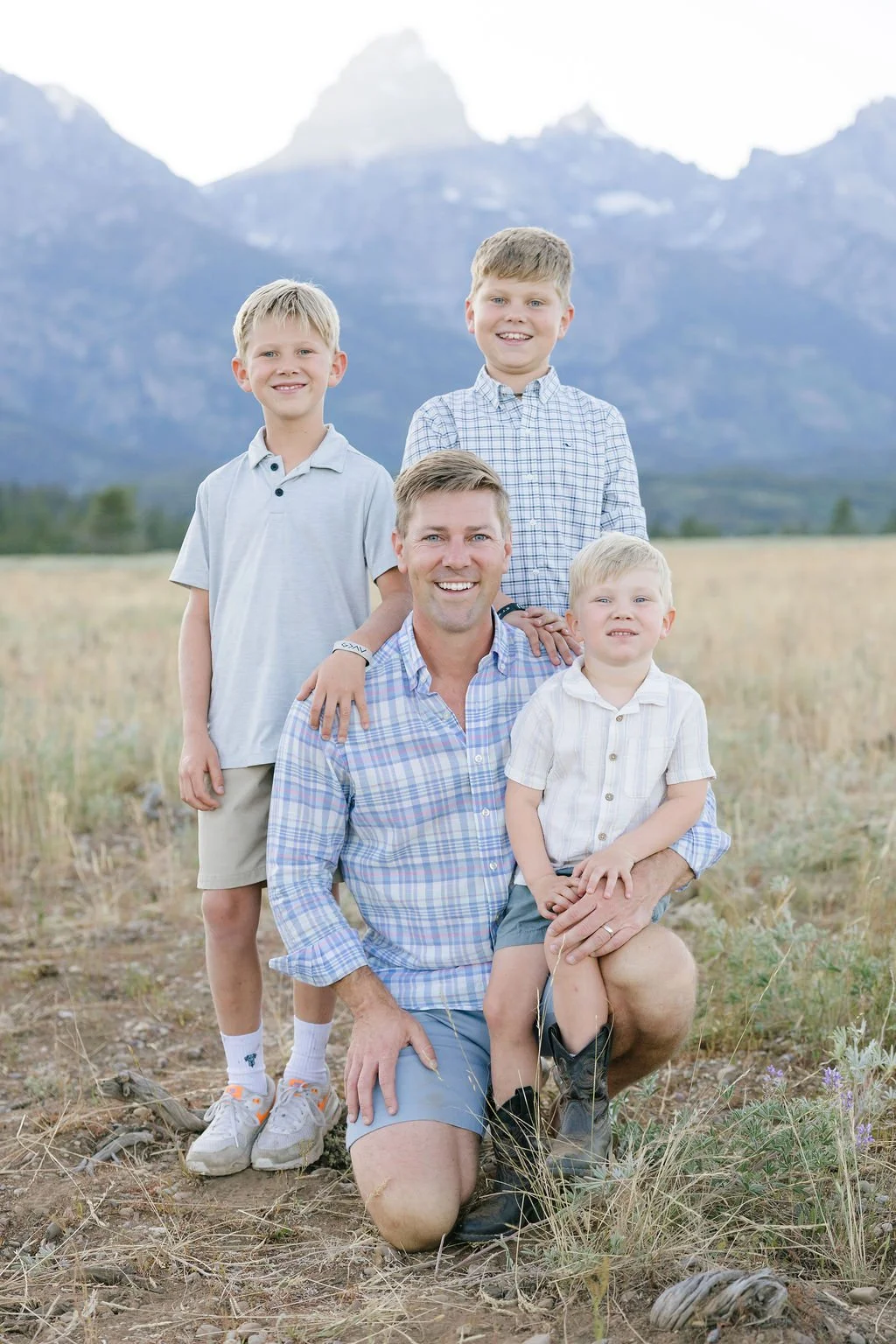  Father with three young boys smiling in a scenic field with the Tetons behind them at Jenny Lake Grand Teton 