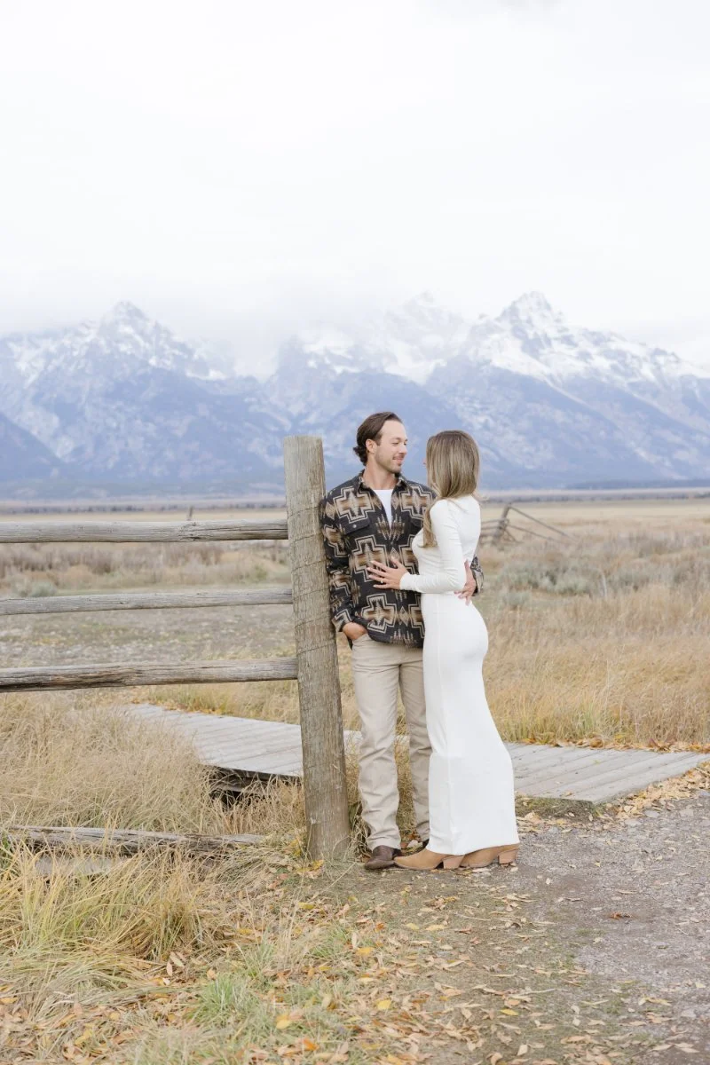  Couple standing by a rustic fence with mountain views during a Jackson WY photographer session 