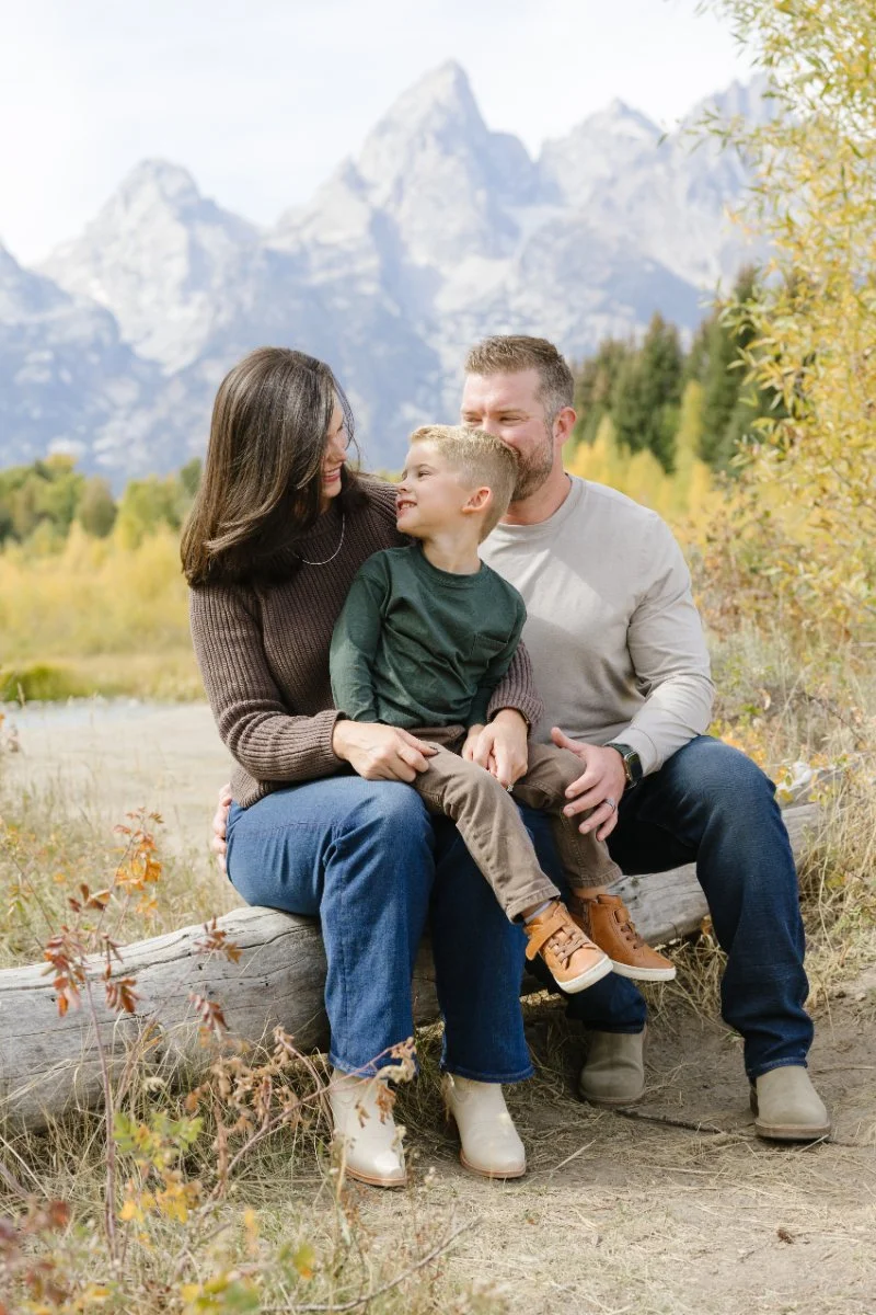  Family cuddling beside the river during Grand Teton wildflowers season in Jackson Hole 