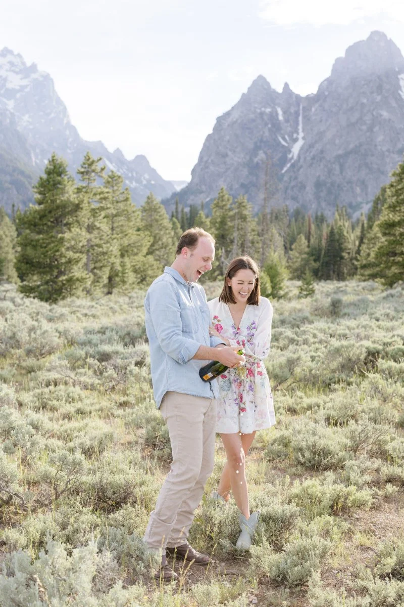  Engaged couple popping champagne in Grand Teton National Park after proposing in one of the most beautiful places to propose in Jackson Hole 