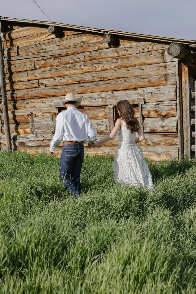  Couple walking beside a historic cabin after their Jackson Hole proposal session in Grand Teton National Park 