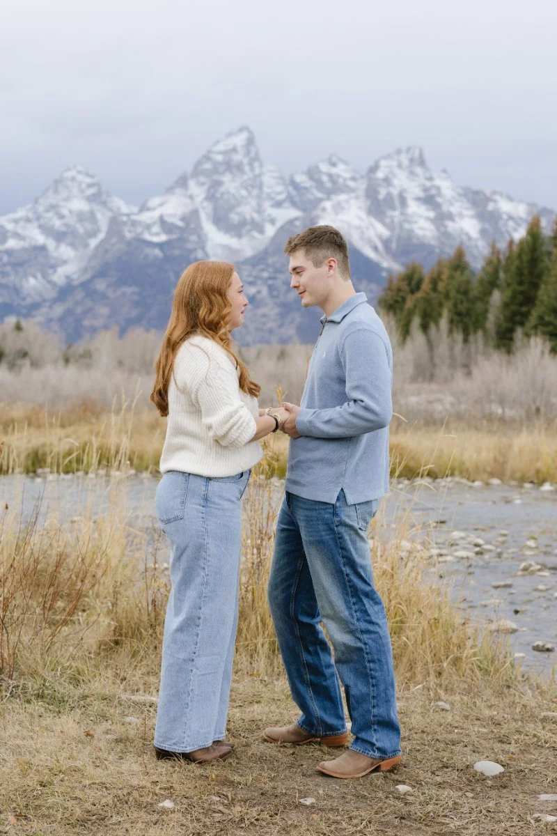  Couple holding hands before a surprise Grand Teton proposal with the Teton mountain range in the background 