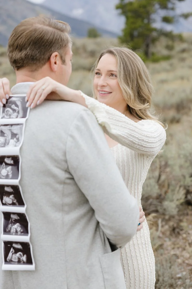  Couple embracing during maternity portraits while displaying their baby's ultrasound photos 