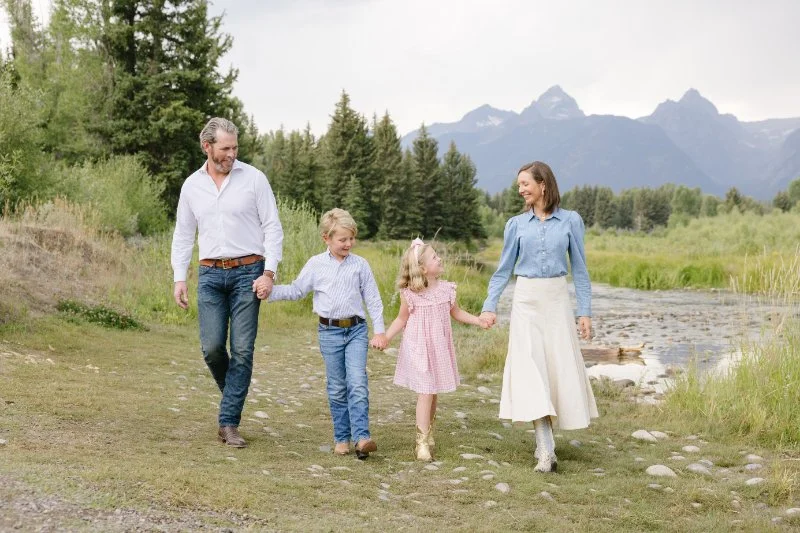 Family walking along a river with mountain views during a session with a Jackson WY photographer