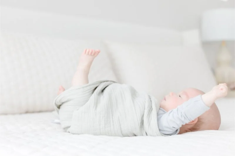Baby boy stretches out of swaddle.