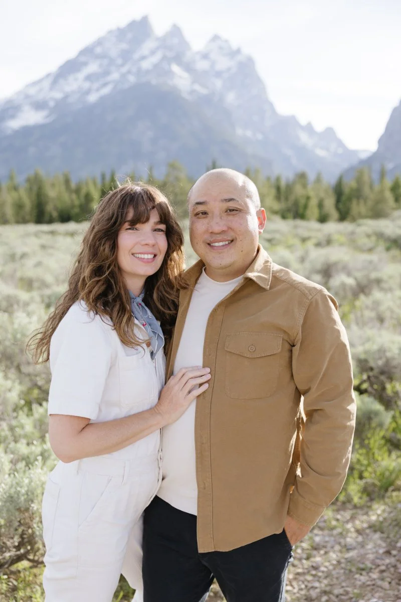 Couple stands together for photograph with the Grand Tetons behind them, celebrating their honeymoon in Jackson Hole with a photo shoot.