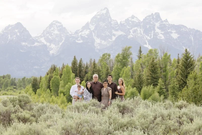 Extended family posing together in a sagebrush meadow with Grand Teton mountains and lush greenery in Jackson Hole during summer