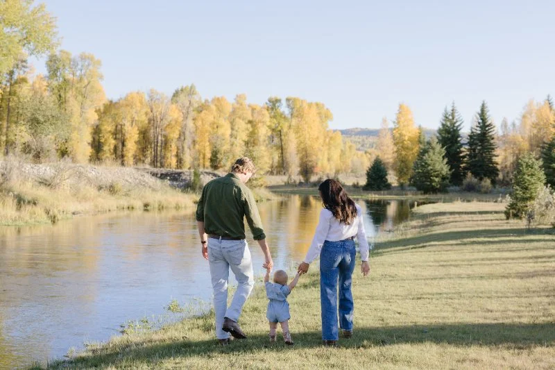 Family walking along a river holding their baby’s hands in a peaceful fall landscape during a Grand Teton family photography session