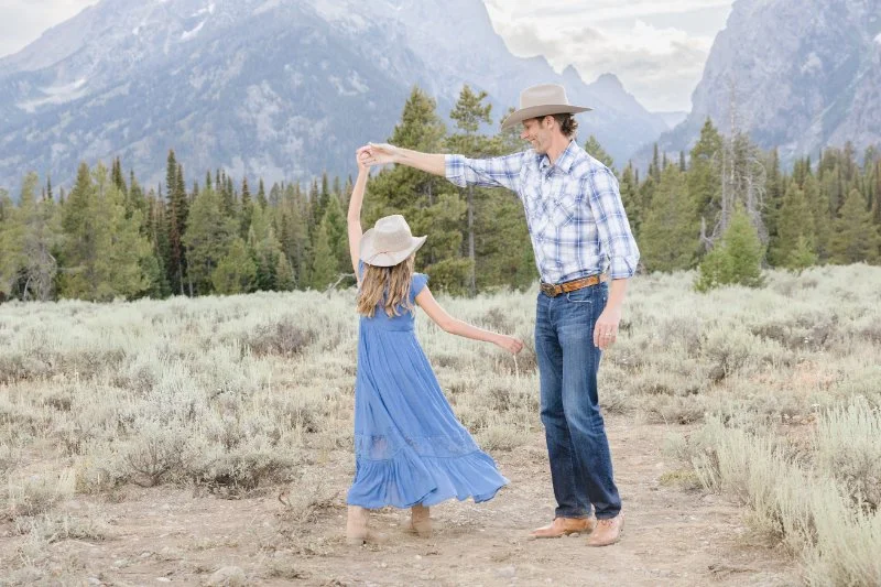 Father twirling his daughter during a family photo session with the Grand Tetons in the background