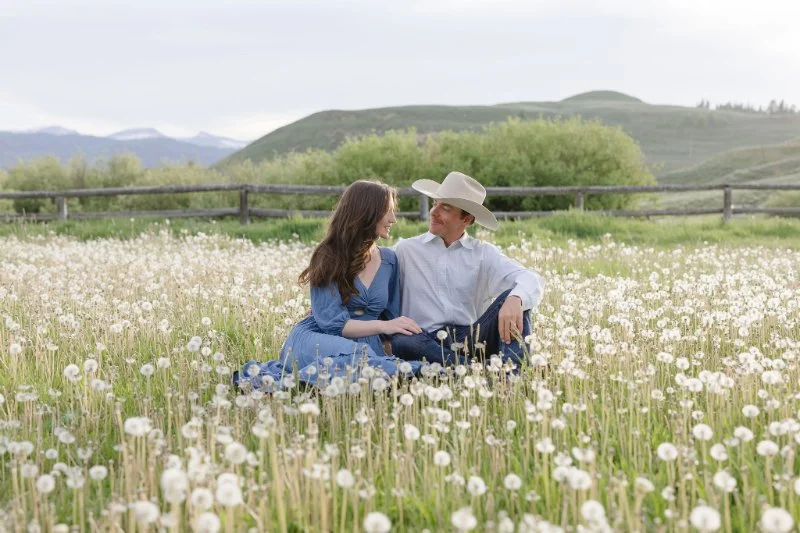 Couple sitting in a wildflower field in Jackson Hole after a romantic proposal surrounded by mountain views in the Tetons