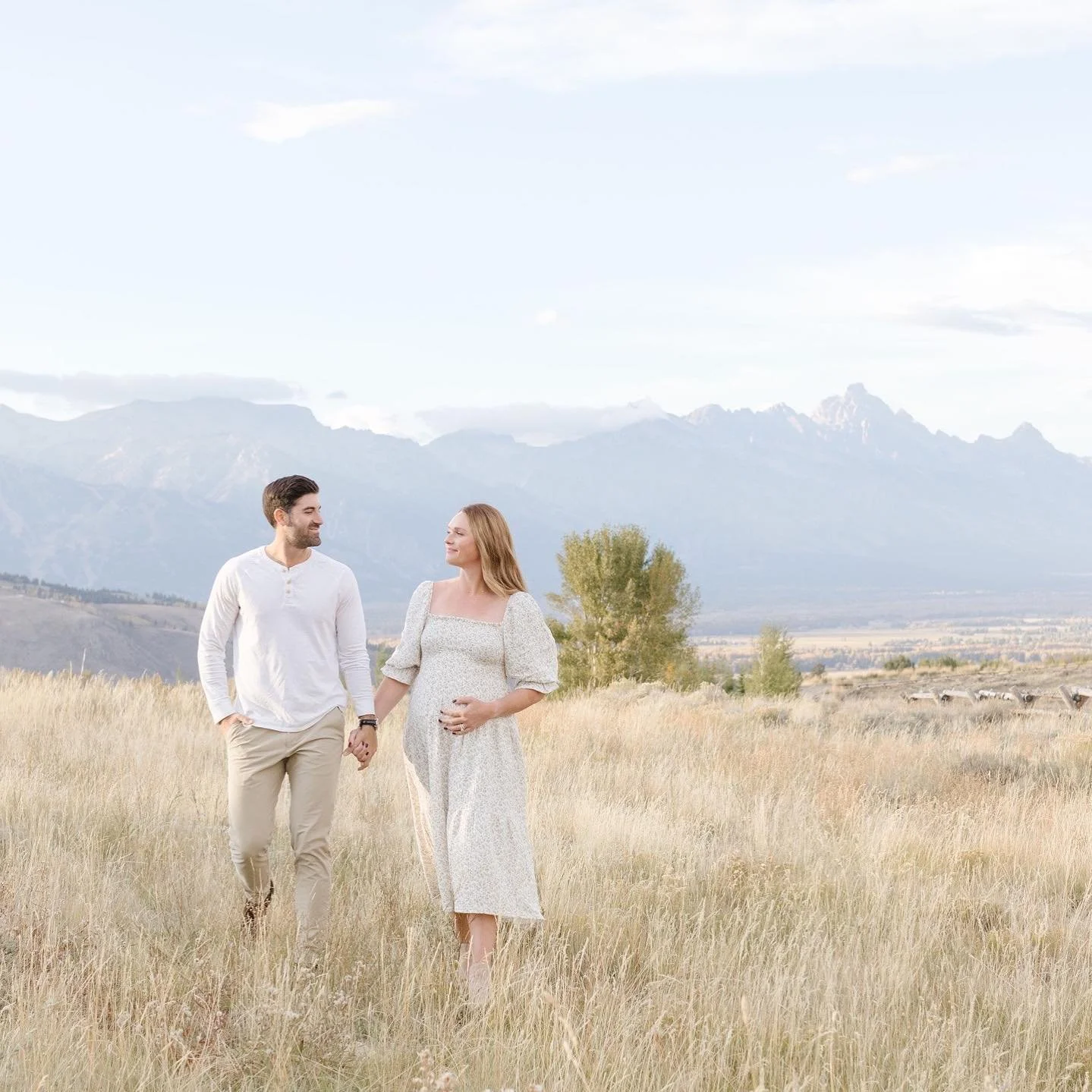 a pregnant woman walking through the grass with her husband